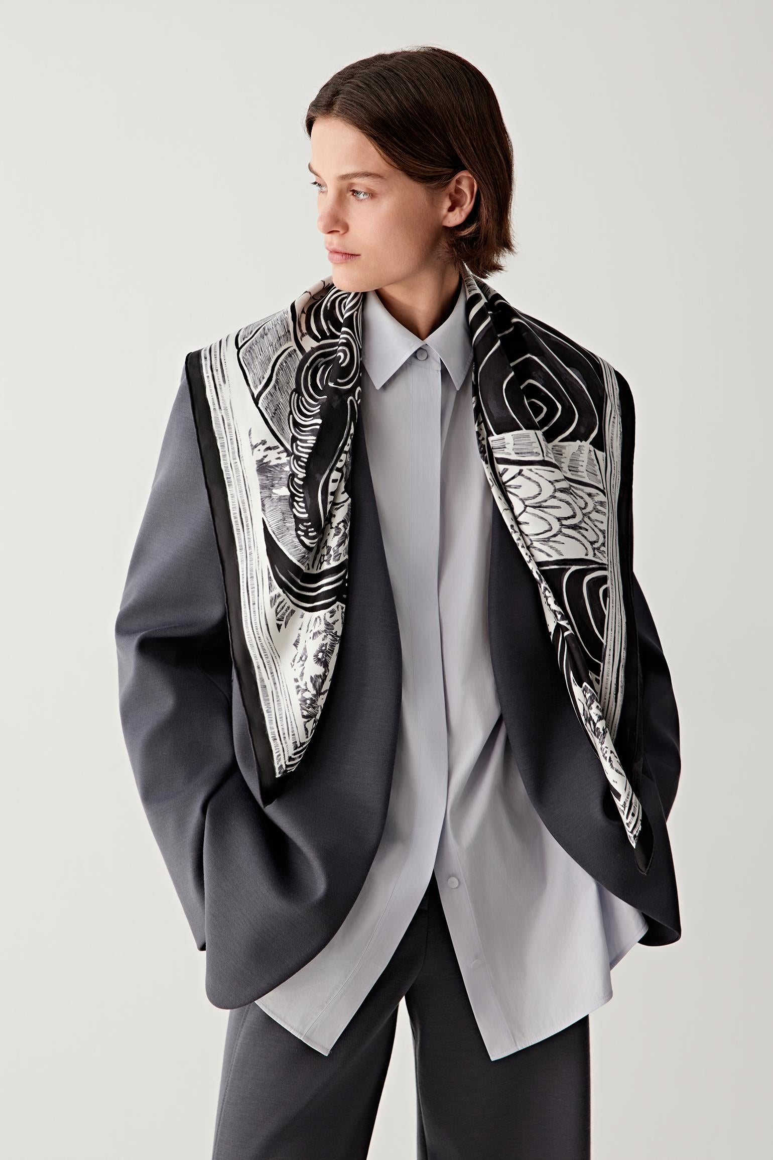 Woman wearing a black and white silk twill scarf over a grey blazer, front view.