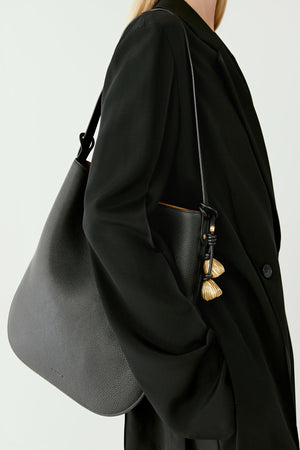Front styling view of a model wearing a hobo bag crafted from grained calf leather in black. The bag’s fluid silhouette rests against the side of the body.