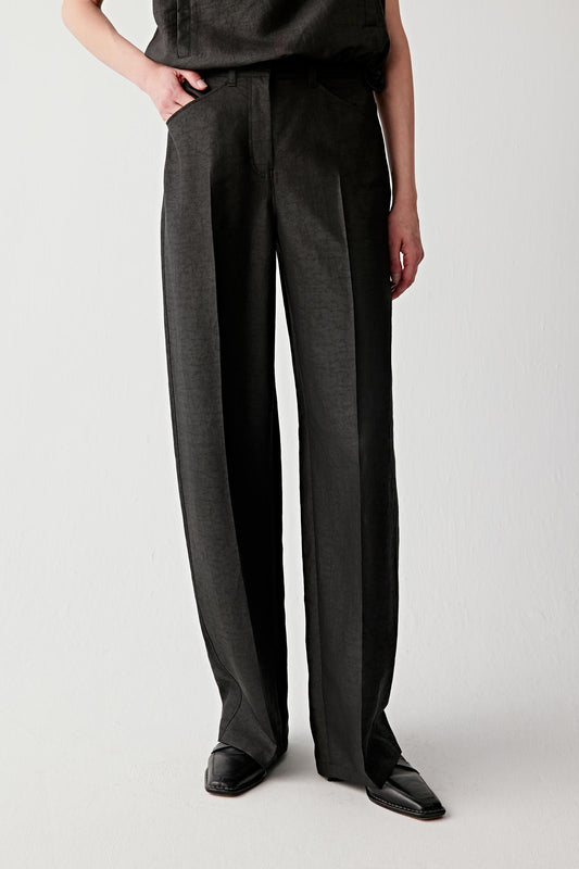 Mid-length front view focusing on the trousers from waist to hem, emphasizing the straight-leg cut, front pleats and the controlled drape of the fabric, with a matte, subtly irregular surface