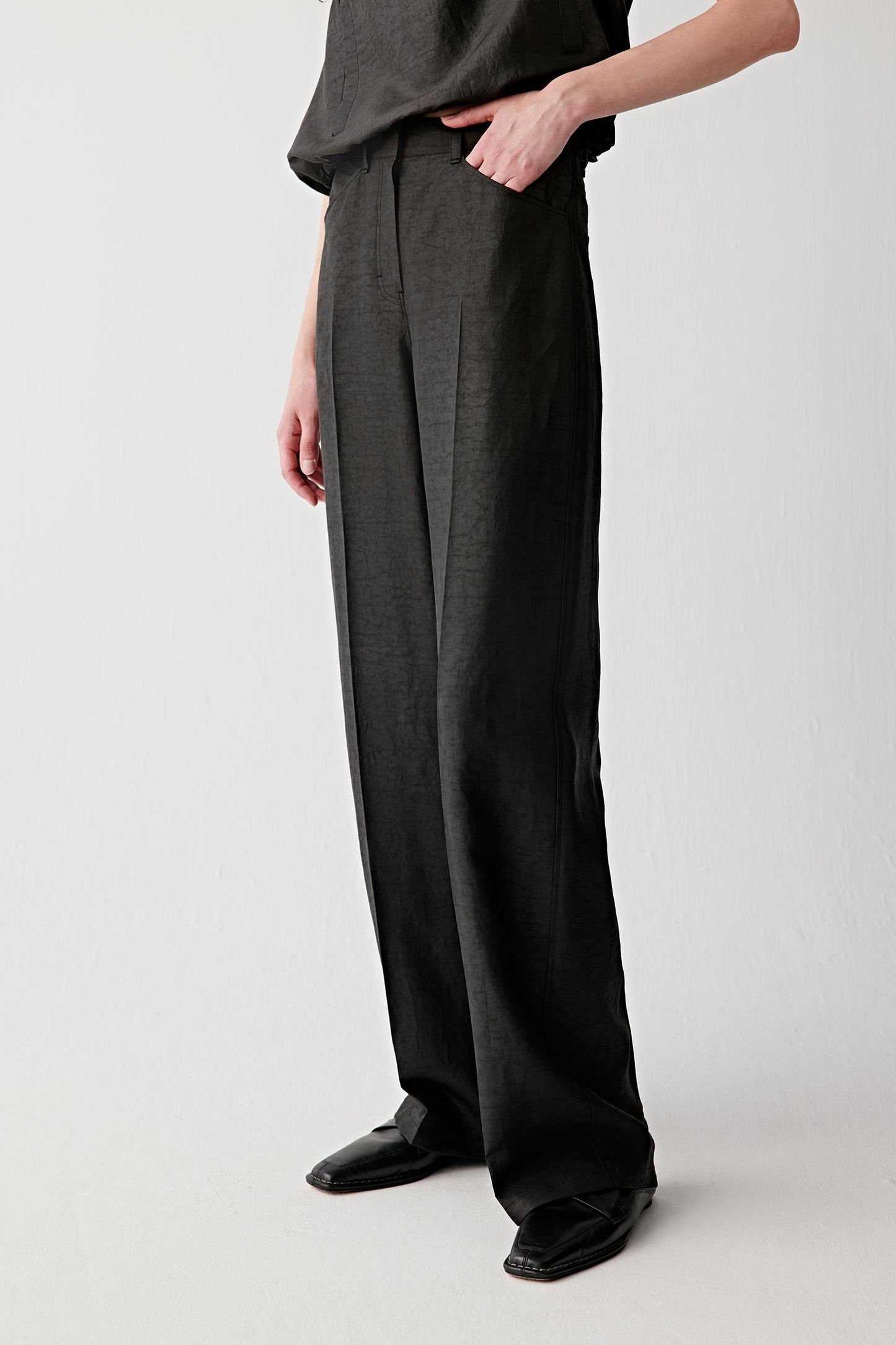Side view showing the trousers in profile, highlighting the vertical fall, the clean outer seam line and the way the fabric holds shape while remaining fluid through movement
