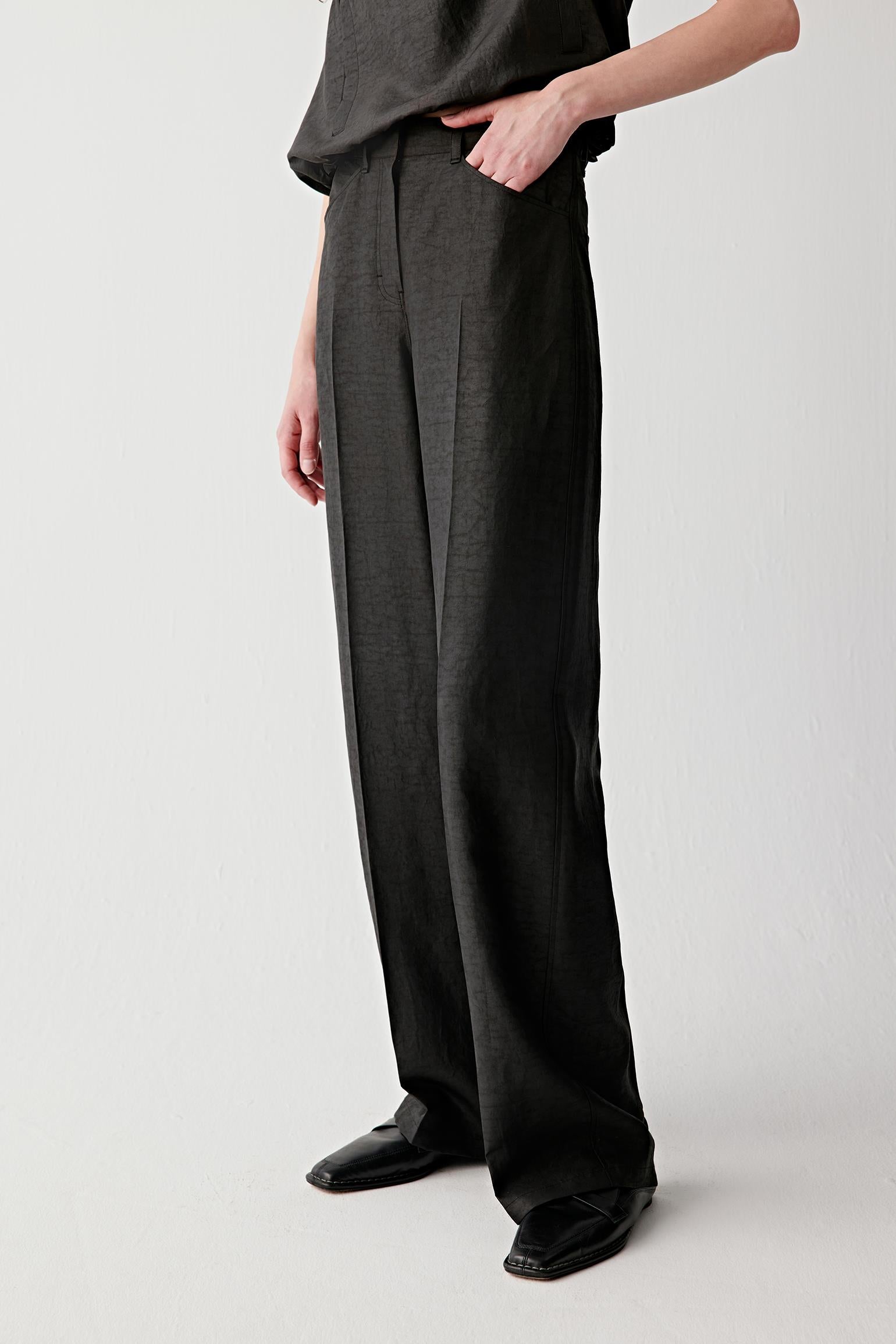 Side view showing the trousers in profile, highlighting the vertical fall, the clean outer seam line and the way the fabric holds shape while remaining fluid through movement