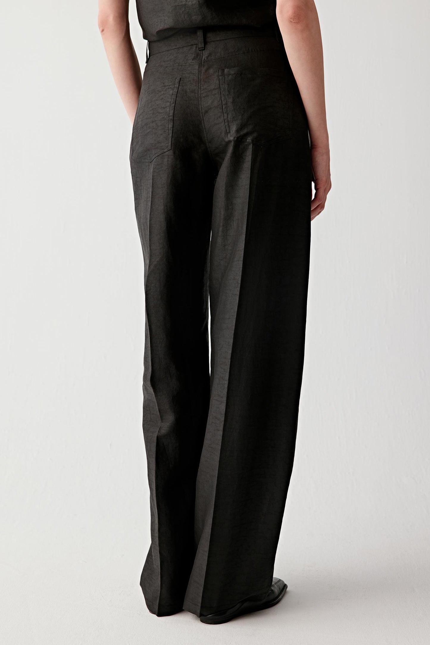 Three-quarter view showing the trousers slightly turned, emphasizing the leg volume, the continuity of the silhouette and the balance between structure and softness in the material