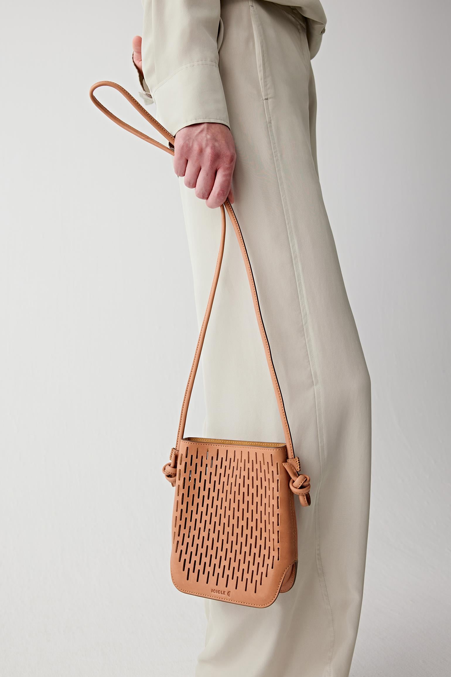 Side view detail showing the camel leather crossbody bag hanging at the hip, emphasizing the openwork perforated texture and soft structure.