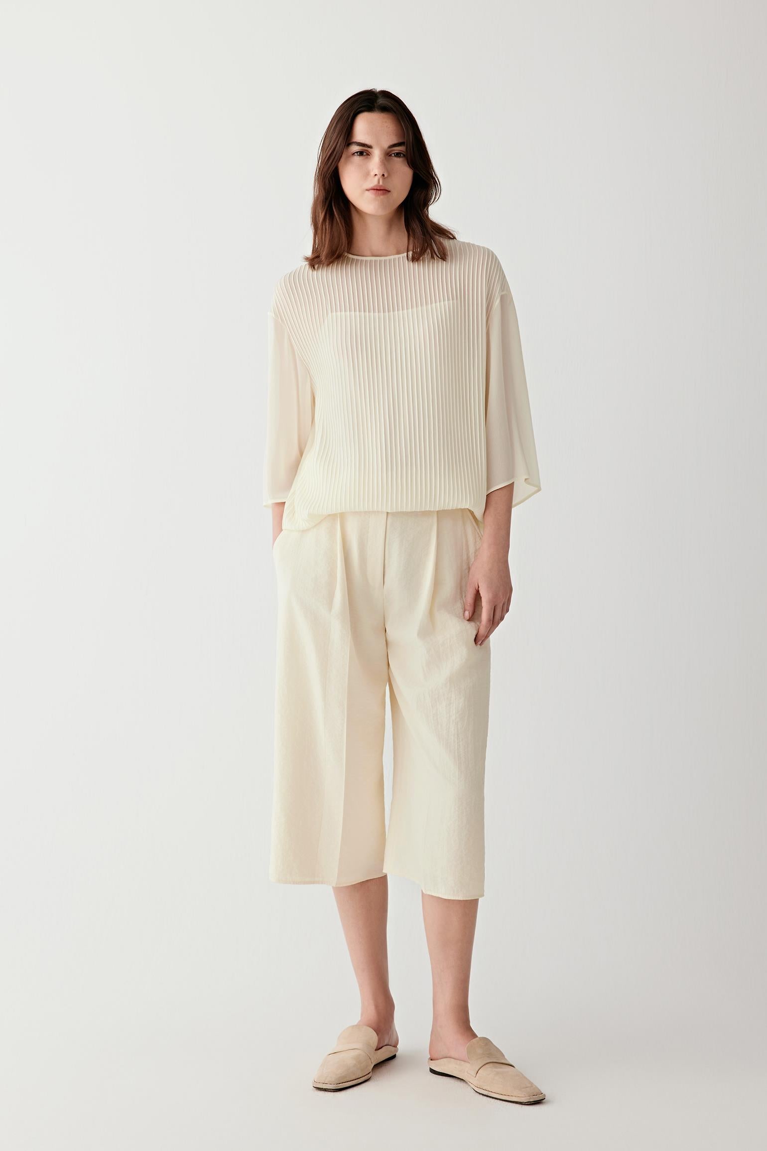 Full-length front view of a woman wearing light cream trousers in silk and nylon seersucker, highlighting the lightly puckered surface, fluid drape and lightweight structure