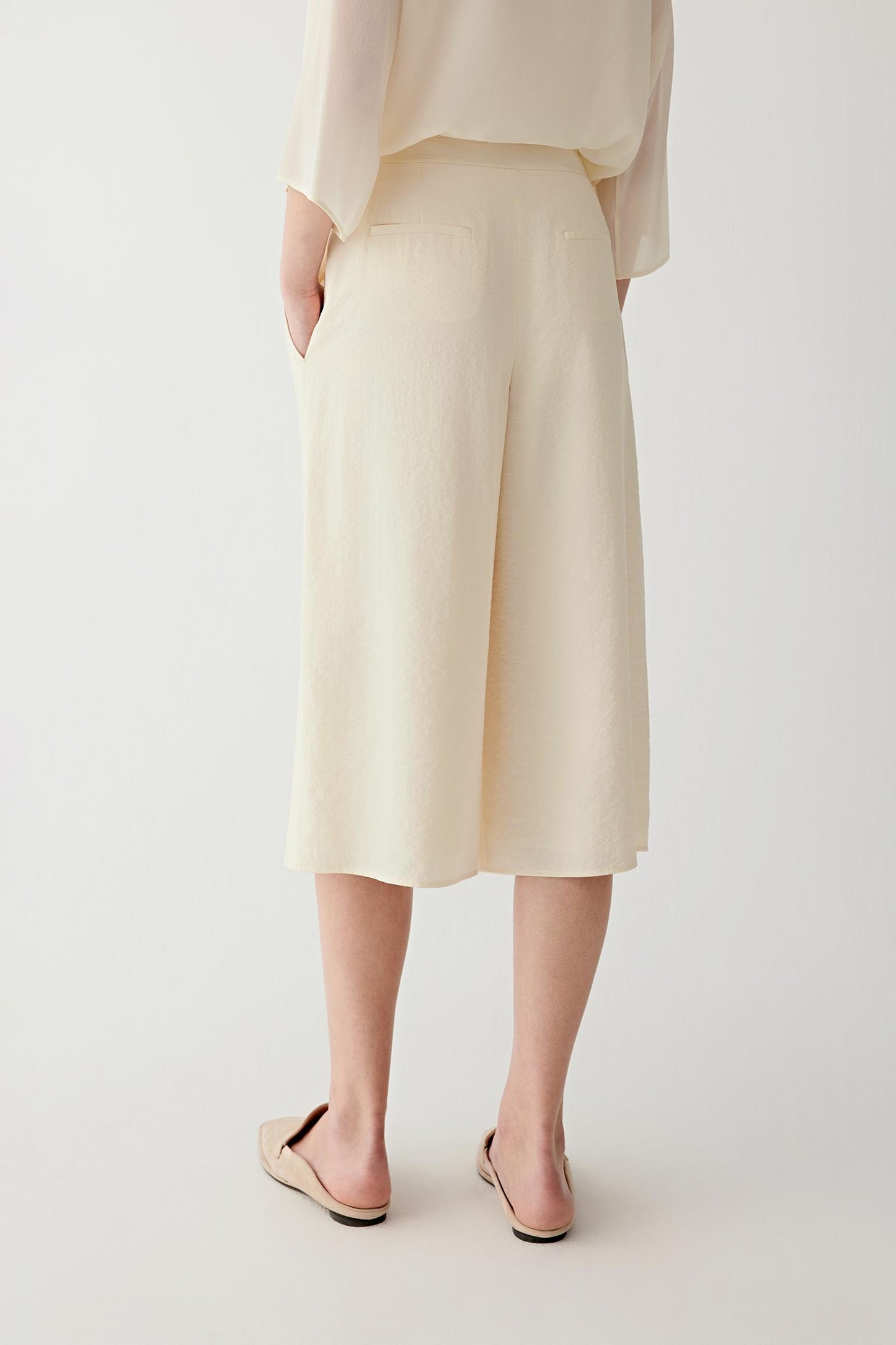 Side or back view highlighting the elongated line and softly textured surface of the trousers