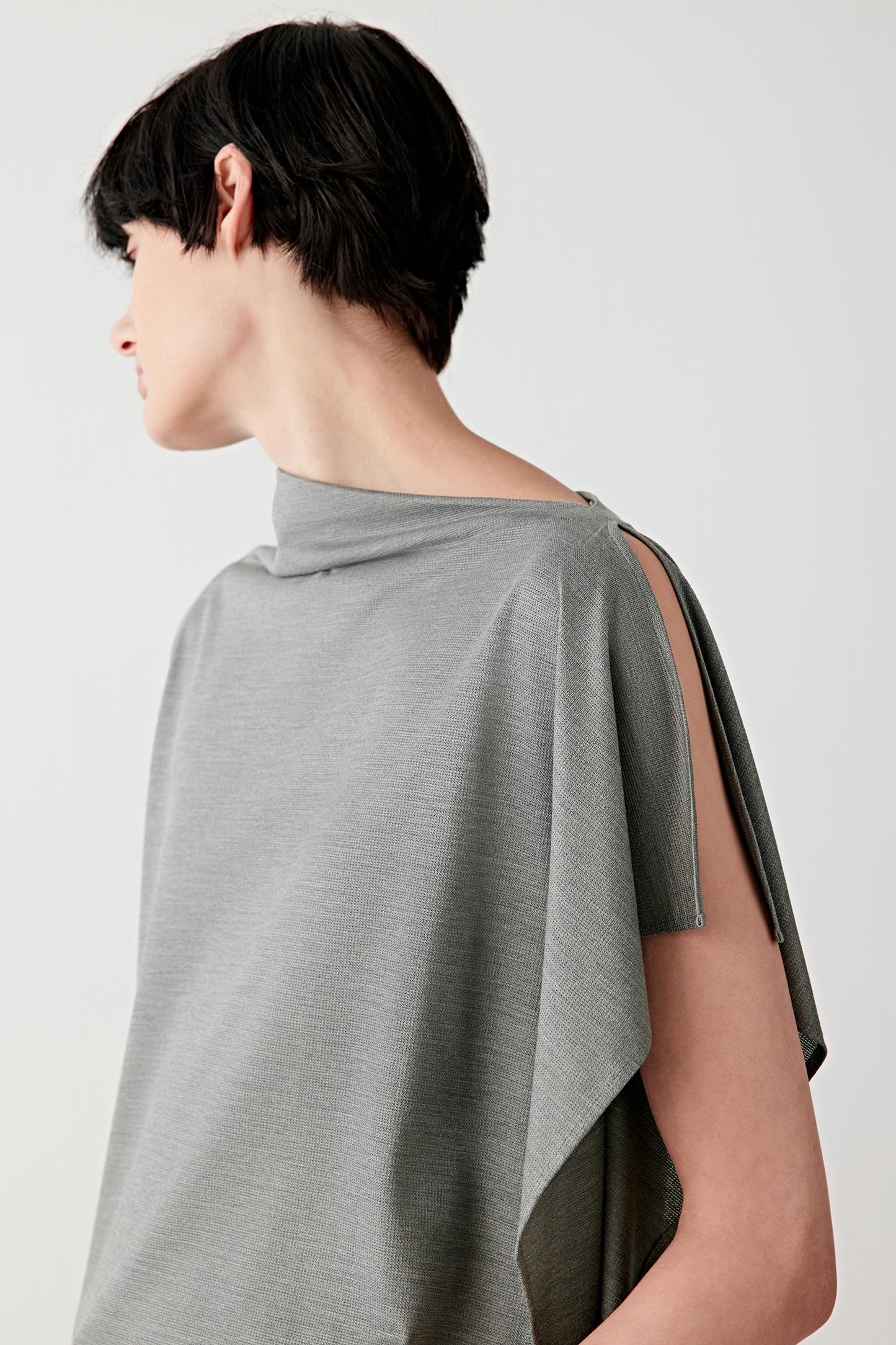 Close-up portrait focusing on the wide neckline extending into the draped collar, detailing the smooth jersey texture, subtle stretch structure and softly gathered folds created by the drape. The mélange effect enhances the depth of the dark grey tone.