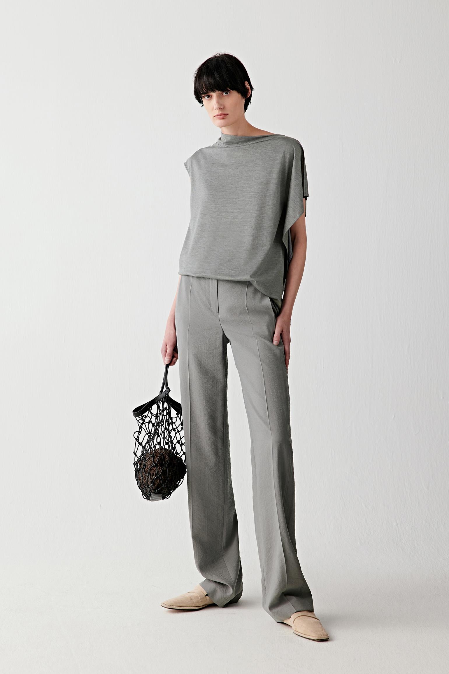 Full-length front view showing the relaxed silhouette shaped by a draped collar, open shoulders and asymmetrical sleeves. The stretch jersey construction follows the movement of the body while maintaining a soft and fluid line.