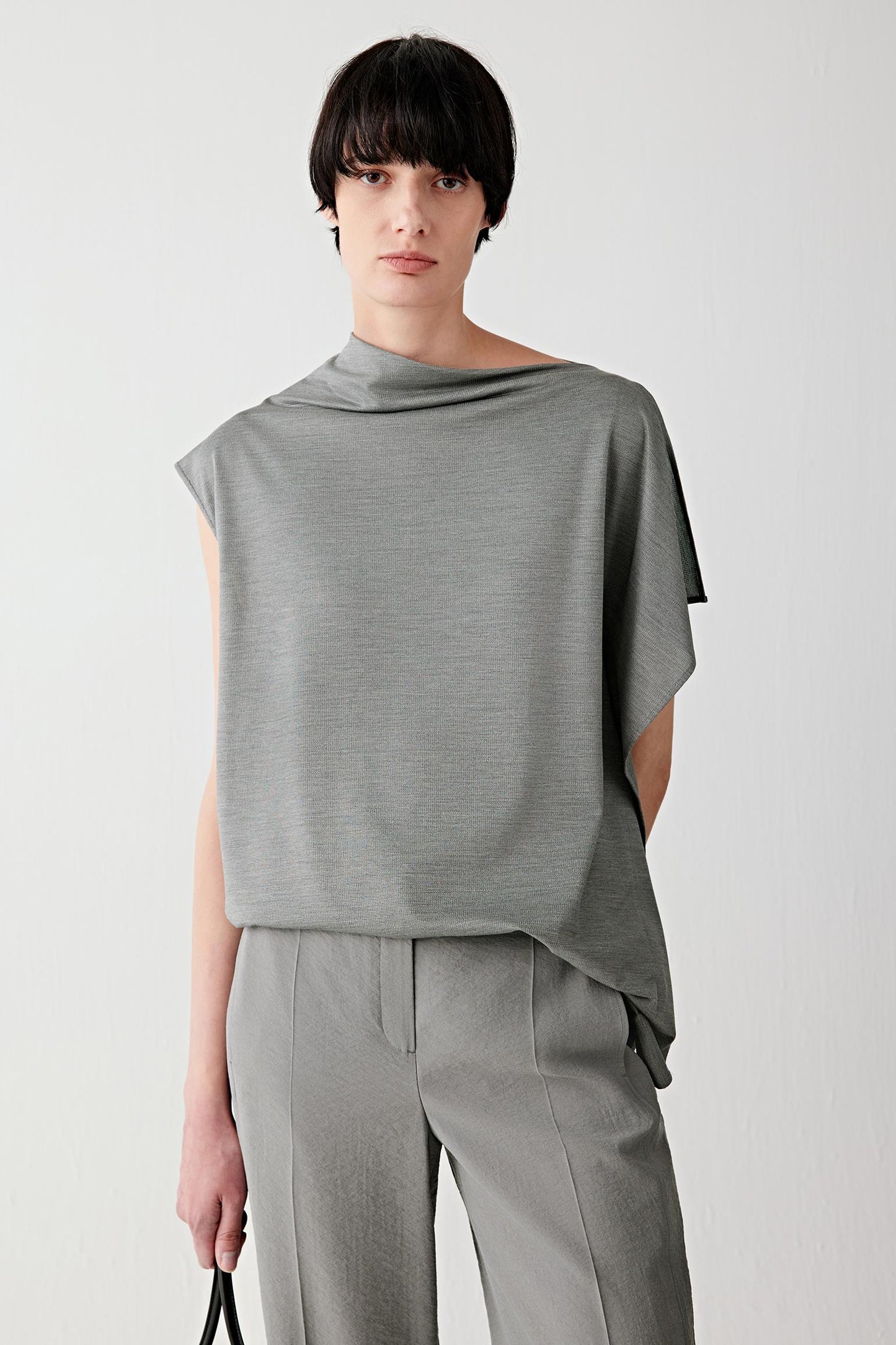 Front view of a woman wearing a dark grey mélange blouse in spun silk stretch jersey, highlighting the smooth matte surface, fluid drape and softly structured jersey construction. The mélange shade introduces subtle tonal variation across the surface.