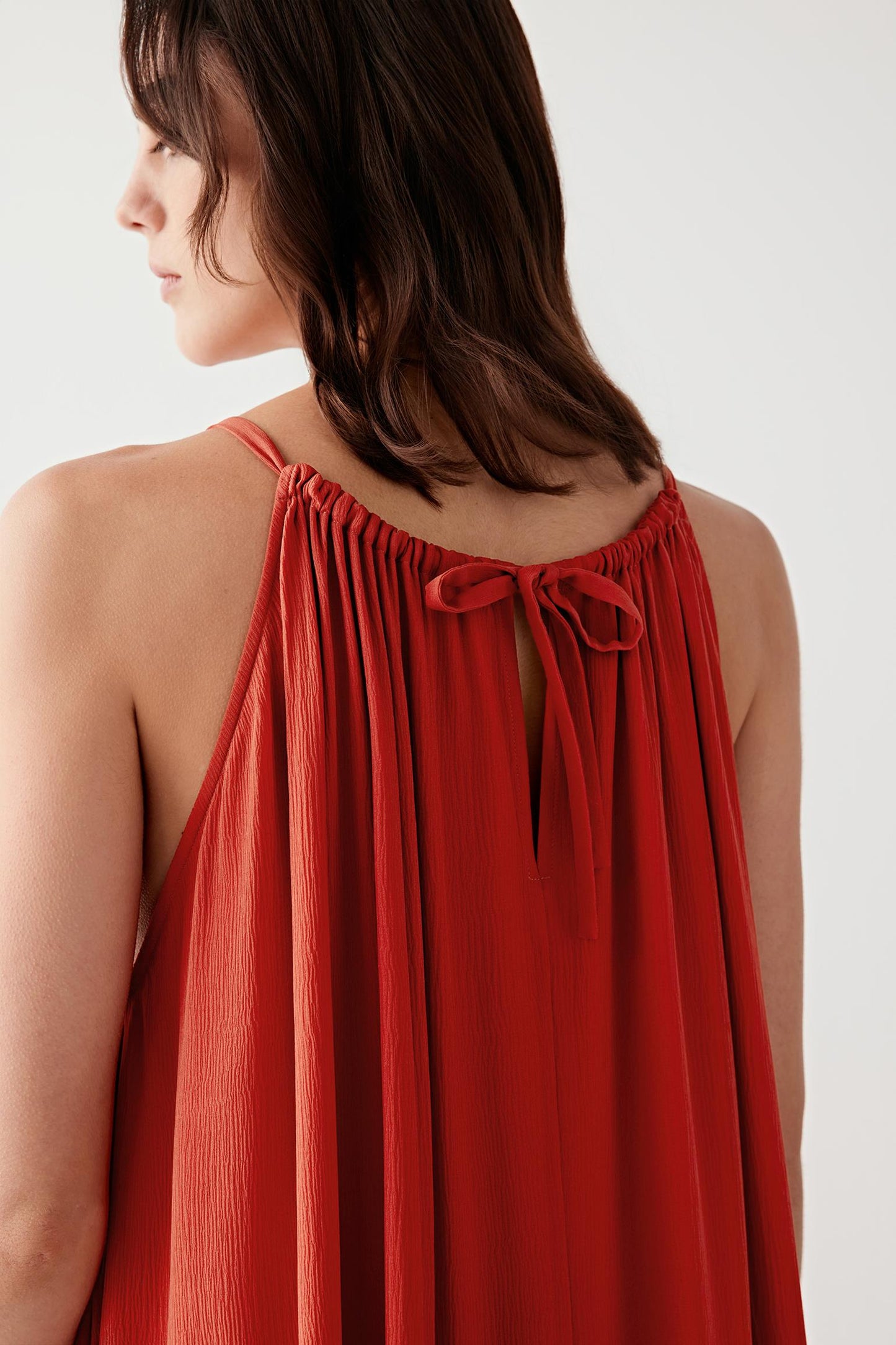 Close-up portrait focusing on the gathered neckline and upper construction, detailing the lightweight mousseline texture, fluid folds and subtle tonal depth of the deep red shade.
