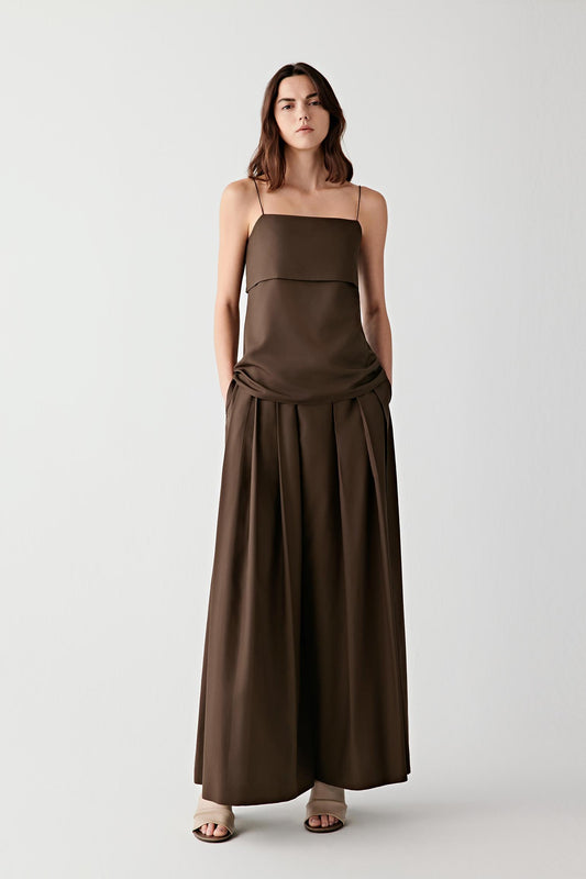 Full-length front view showing the elongated silhouette and thin shoulder straps, emphasizing the layered front panel construction and the fluid movement created through the lower part of the garment. The softly flared line introduces subtle volume while maintaining a clean and continuous silhouette.