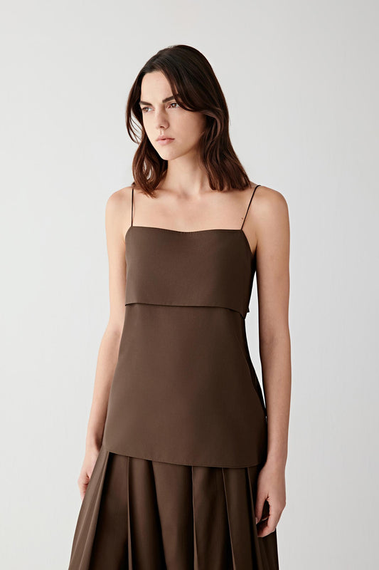 Front view of a woman wearing a deep brown blouse in spun silk poplin, highlighting the smooth compact surface, lightweight structure and fluid drape. The fabric reveals a soft sheen and a dense yet fluid construction that falls cleanly along the body.
