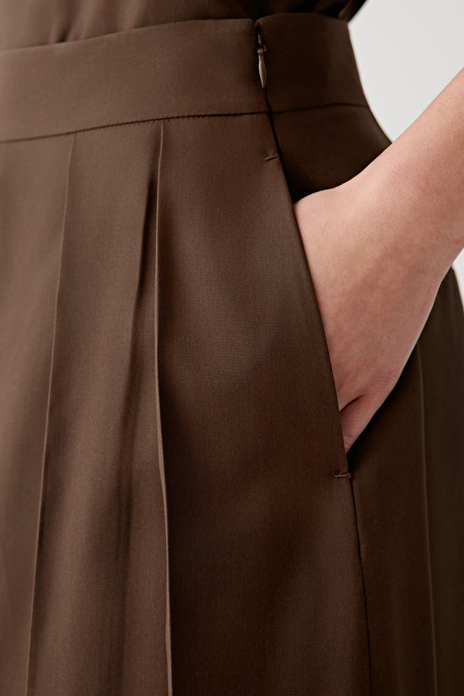 Close-up of the side pocket area showing the smooth matte surface, fluid hand and subtle depth of the dark brown fabric. The image emphasizes the clean pocket construction and refined finishing details of the garment.