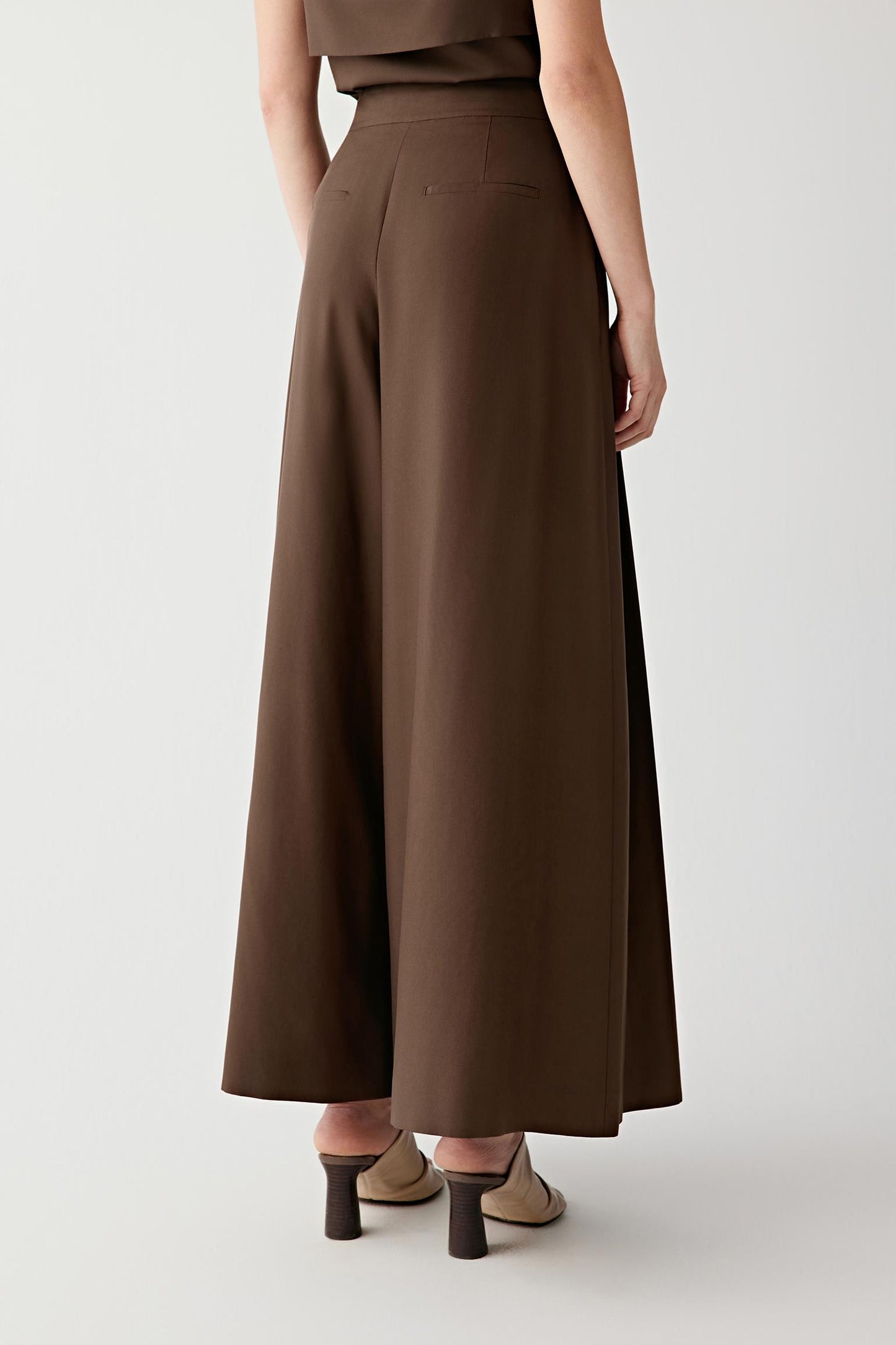 Back view showing the wide-leg silhouette and the way the fabric falls evenly through the length of the garment. The image highlights the smooth surface, fluid drape and clean construction of the trousers.
