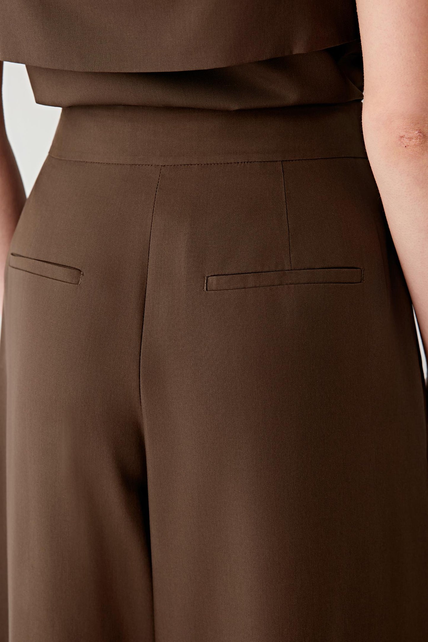 Close-up of the waistband and front pleat construction, revealing the tailored finishing, clean lines and compact texture of the spun silk poplin. The image highlights the precise shaping that defines the upper silhouette.