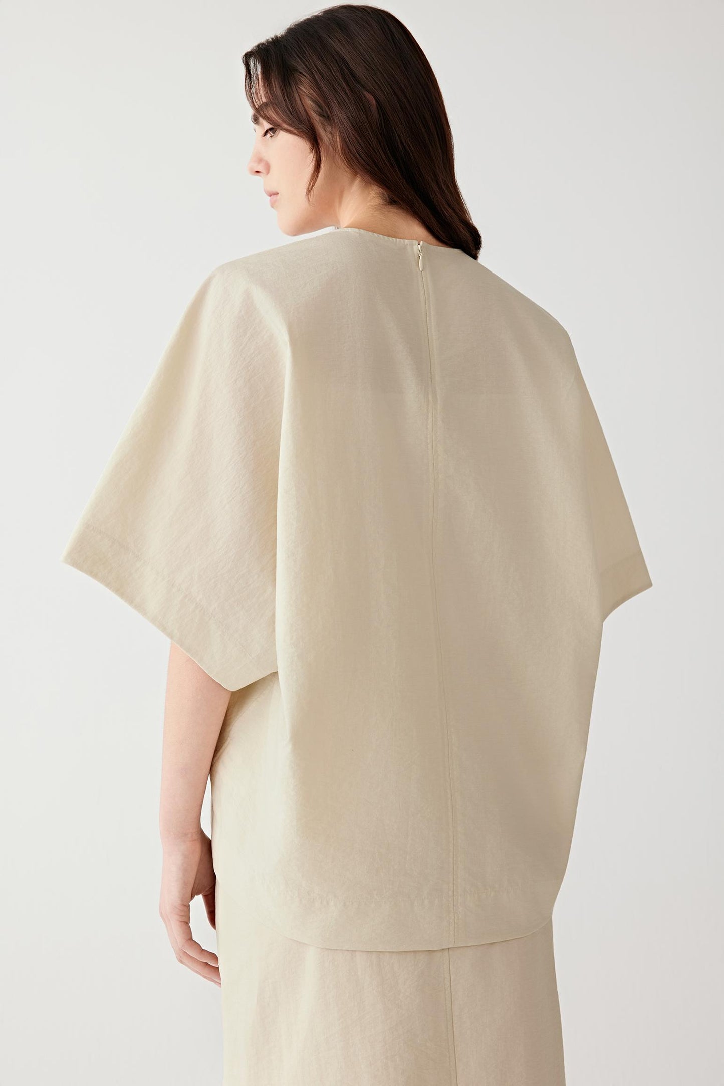 Close-up portrait focusing on the round neckline and upper construction, detailing the crinkled texture and matte finish of the poplin surface