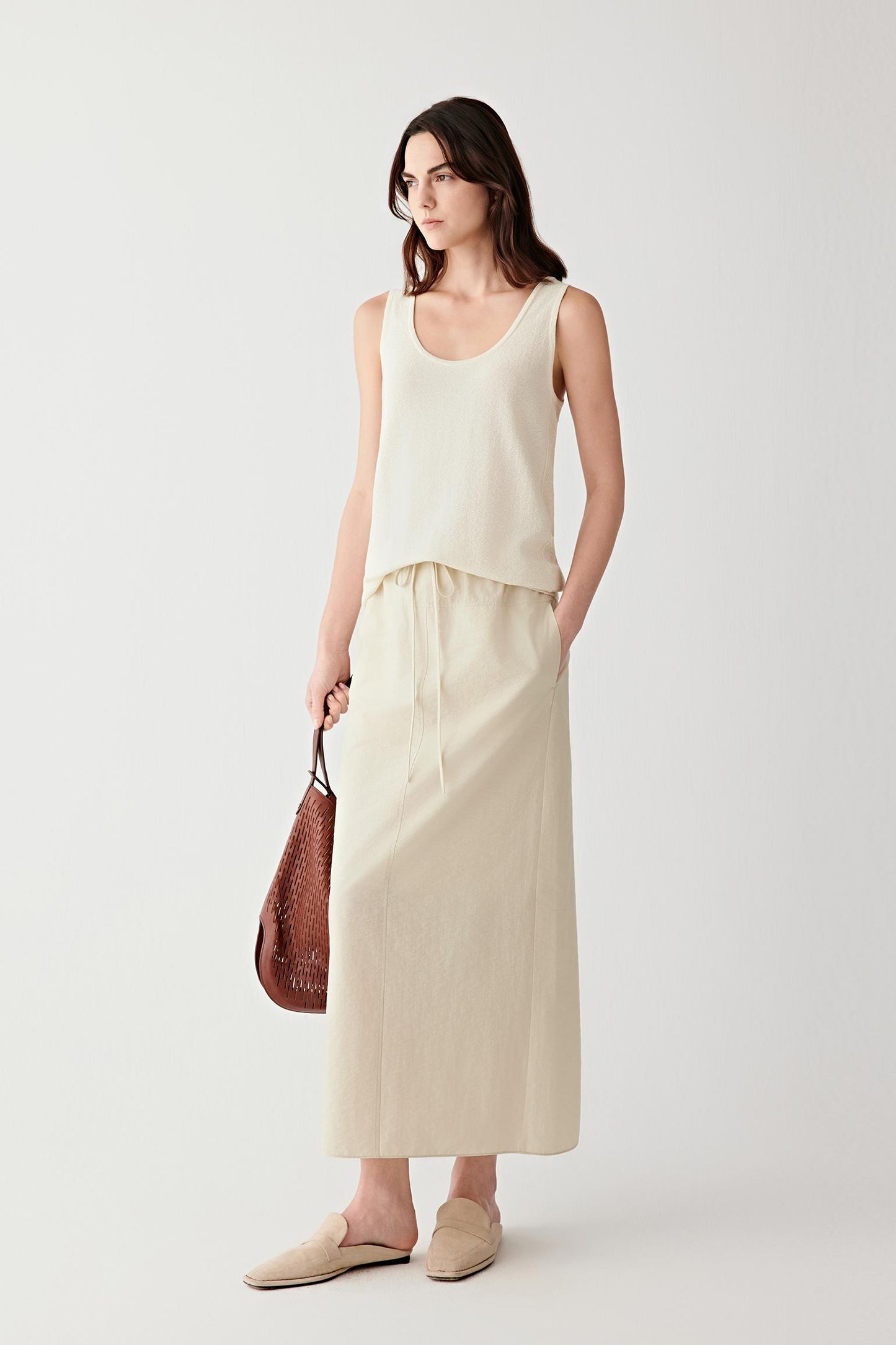 Full-length front view of a woman wearing an off-white sleeveless top in silk and nylon, highlighting the fine knit structure, subtle transparency and fluid drape