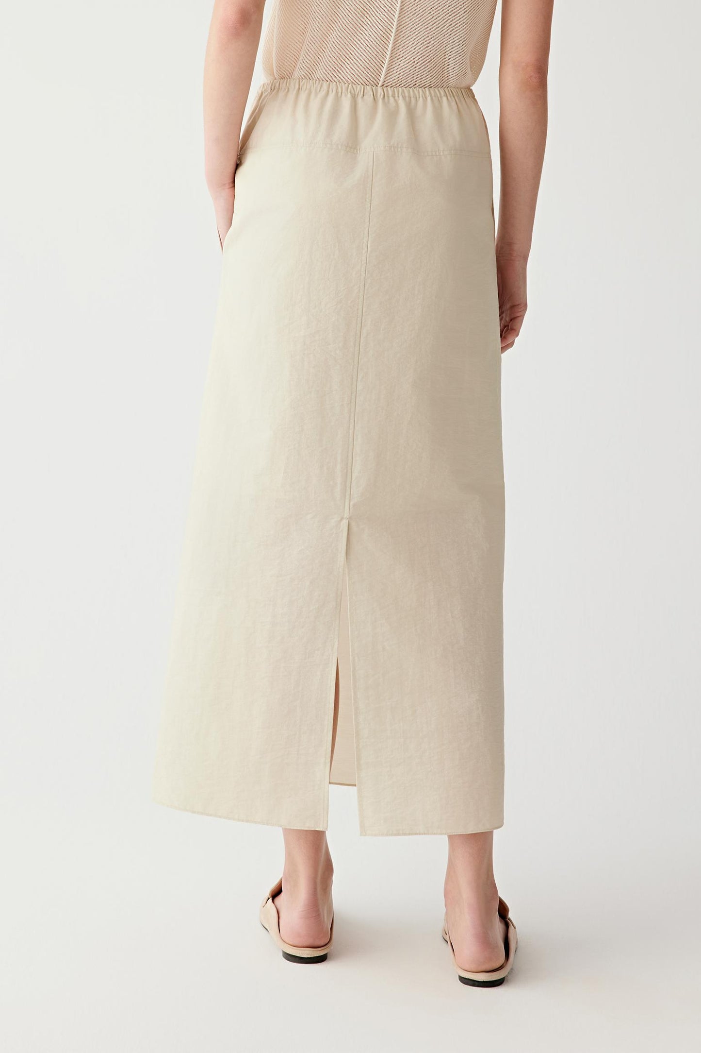 Back view showing the clean silhouette and fluid movement of the skirt. The lightweight crinkled poplin falls naturally from the gathered waistband, while the back slit introduces ease of movement and subtle volume through the lower section.