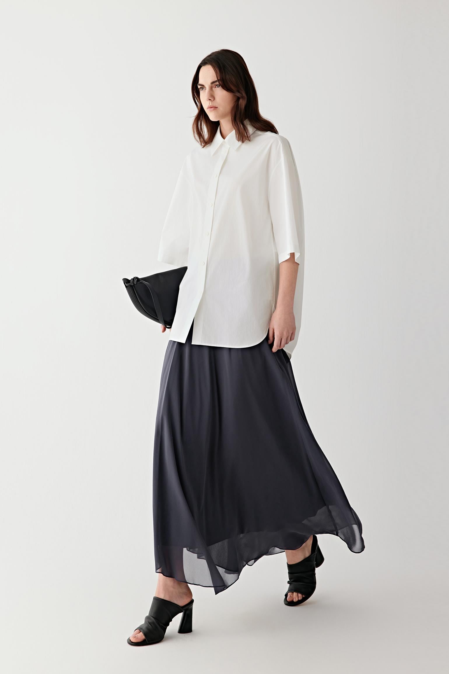 Full-length front view of a woman wearing a deep blue silk georgette skirt, highlighting the fluid drape, lightweight structure and softly matte surface