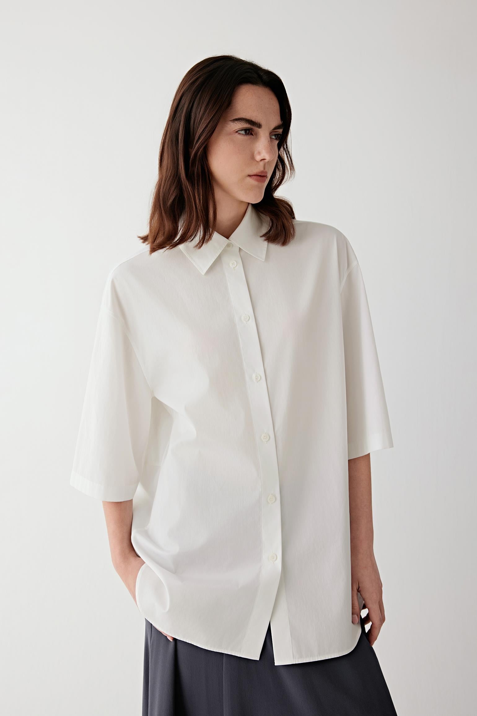 Front view of a woman wearing a white cotton poplin shirt, highlighting the smooth crisp surface, lightweight structure and clean silhouette