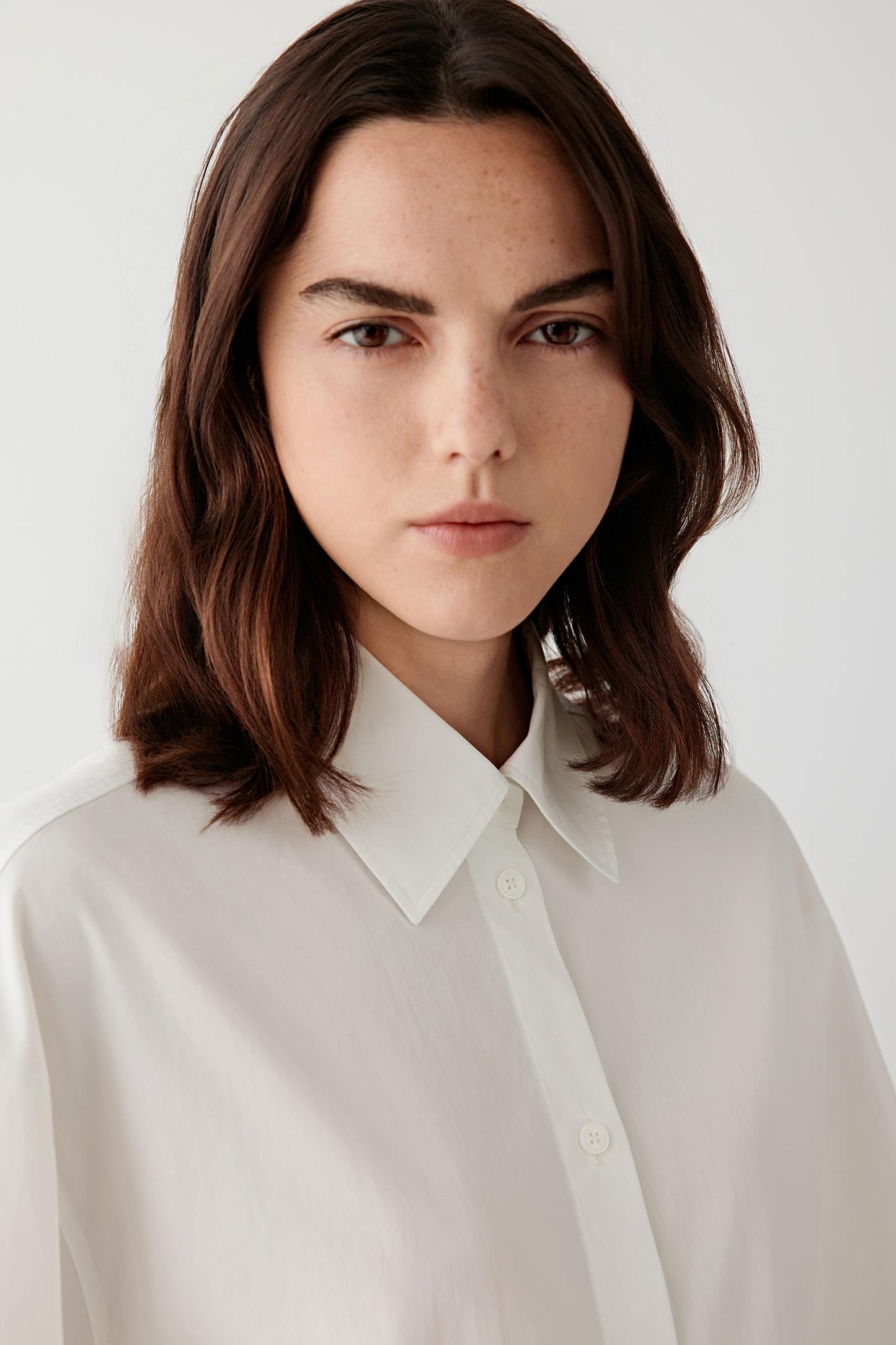 Close-up portrait focusing on the collar and button fastening, detailing the crisp woven surface and matte finish of the cotton poplin