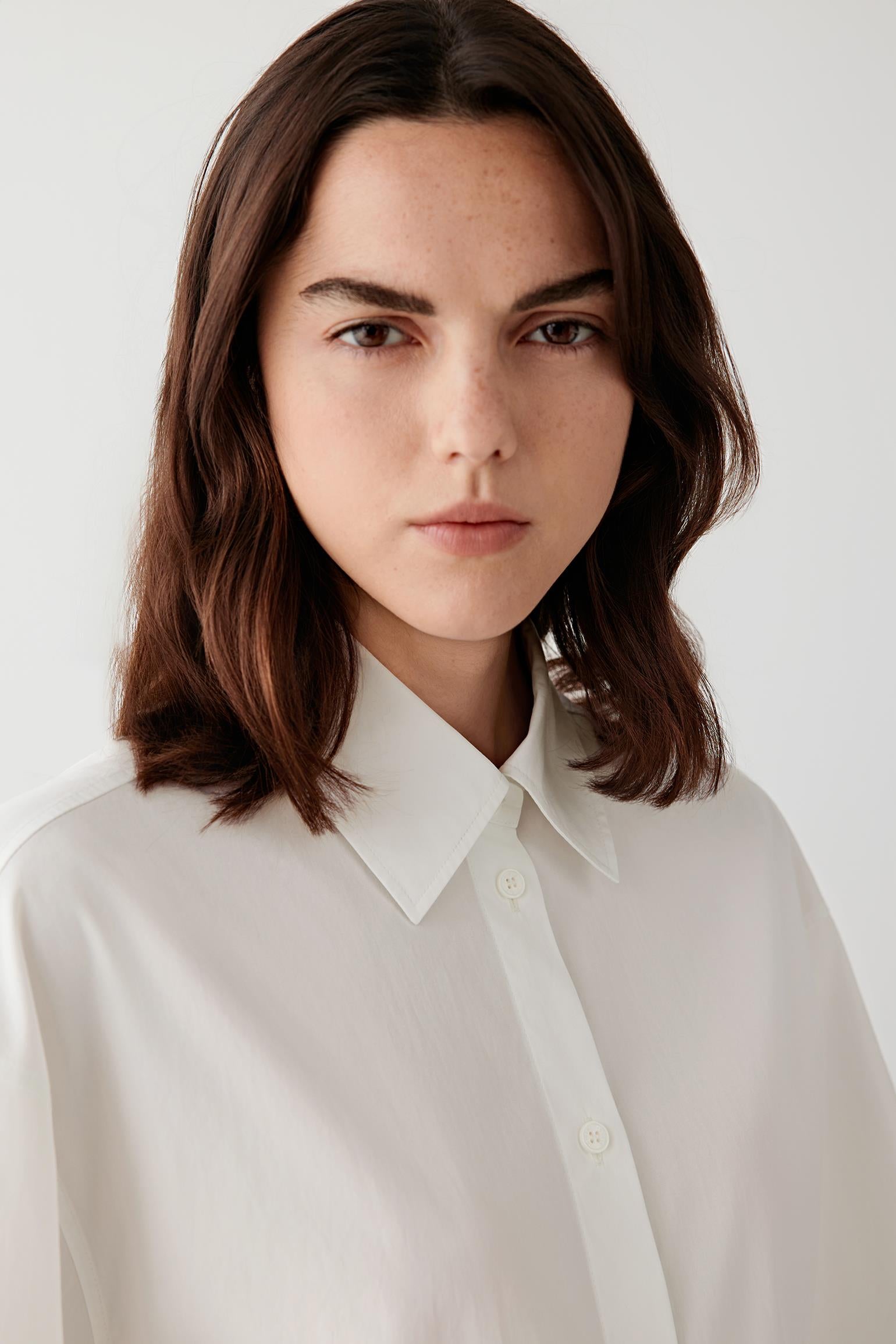 Close-up portrait focusing on the collar and button fastening, detailing the crisp woven surface and matte finish of the cotton poplin