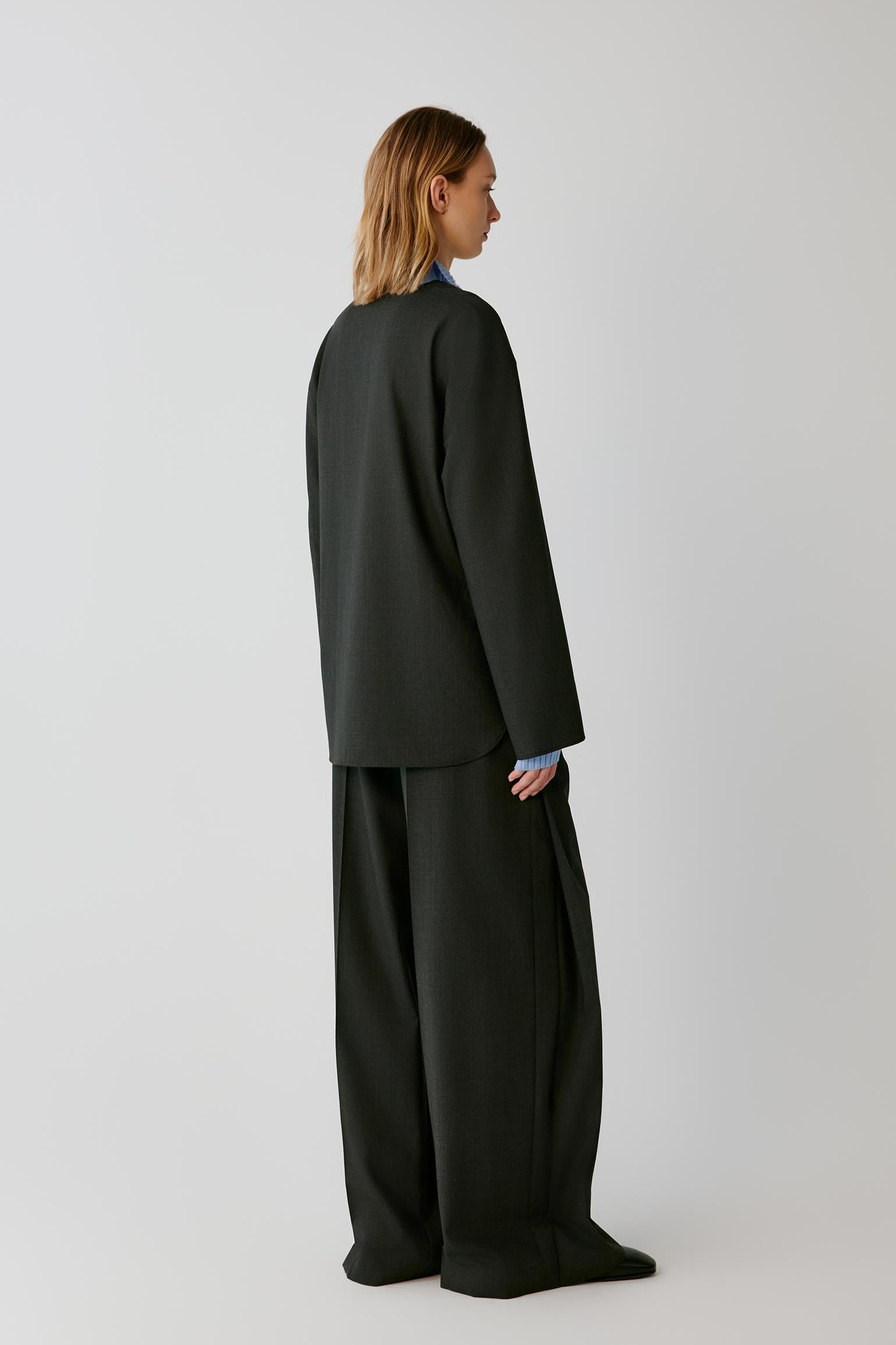 A model shown from the back wearing a black wide-sleeve top and matching wide-leg trousers against a light gray studio background.