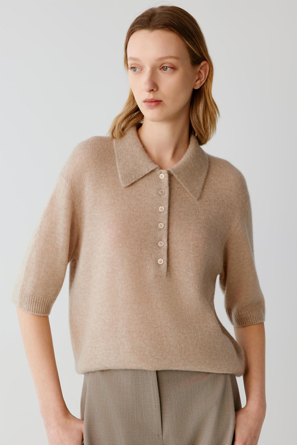 Front view of a woman wearing a beige cashmere and silk top, showing the pointed collar, partial button placket and elbow-length sleeves.