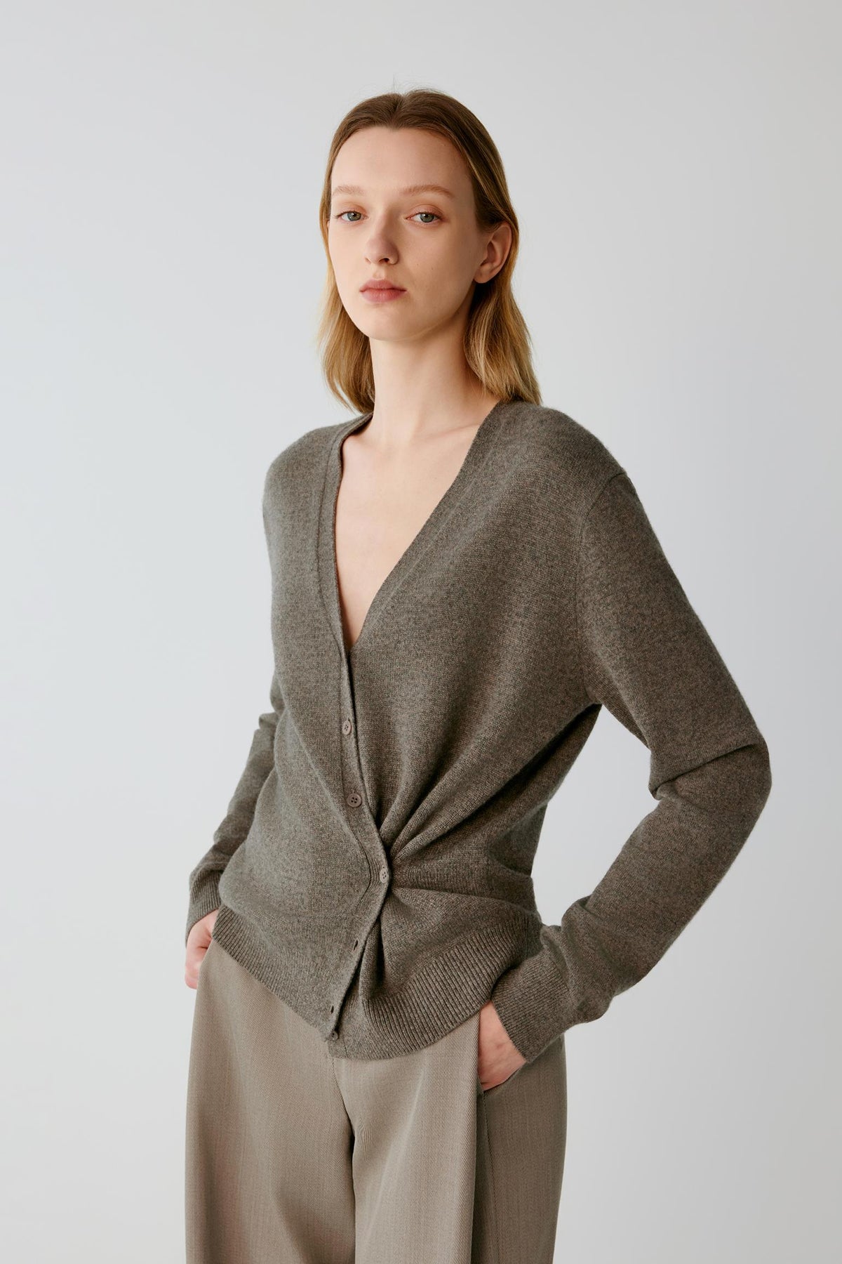 Three-quarter view highlighting the V-neckline, asymmetric wrap construction and gathered detailing of the taupe cashmere cardigan.