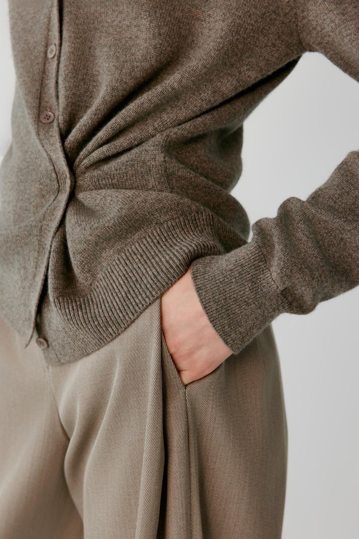 Close-up highlighting the gathered waist detailing, wrap construction and fine-knit texture of the taupe cashmere cardigan.