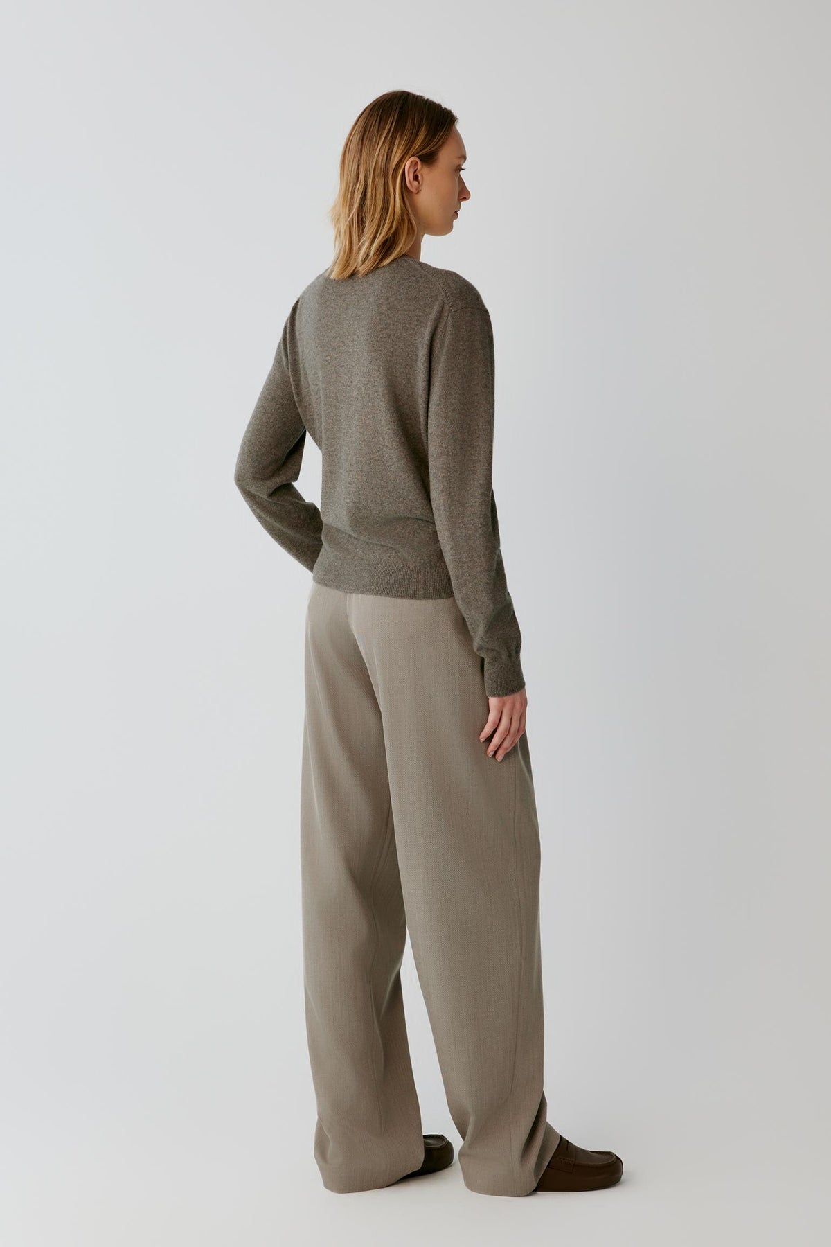 Back full-length view of a woman wearing the taupe cashmere wrap cardigan, showing the clean back and long sleeves.
