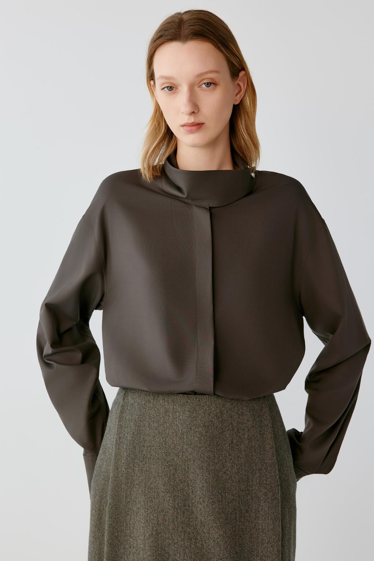 Front view highlighting the stand collar, concealed front placket and long sleeves of the walnut brown silk poplin shirt.
