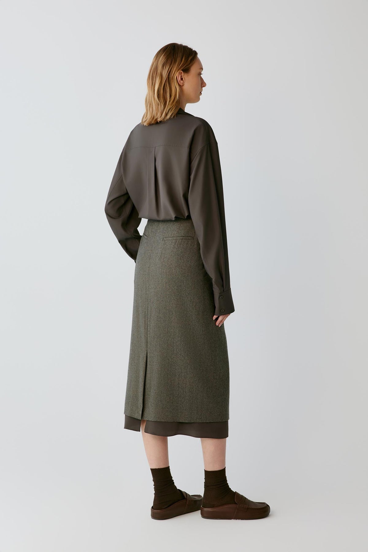 Back view of a woman wearing the walnut brown silk poplin shirt, showing the back pleat and fluid silhouette.