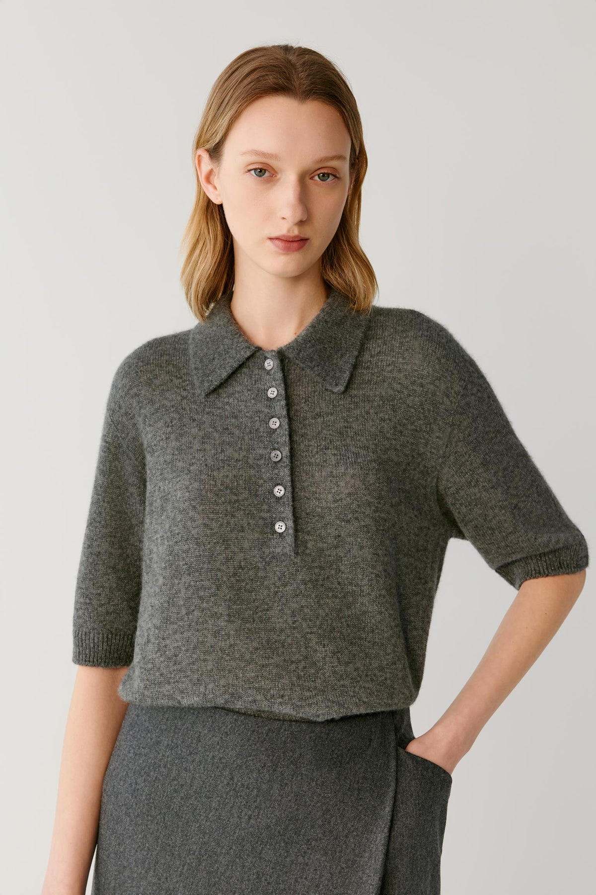 Front view of a woman wearing a smoke grey cashmere and silk top, showing the pointed collar, partial button placket and elbow-length sleeves.
