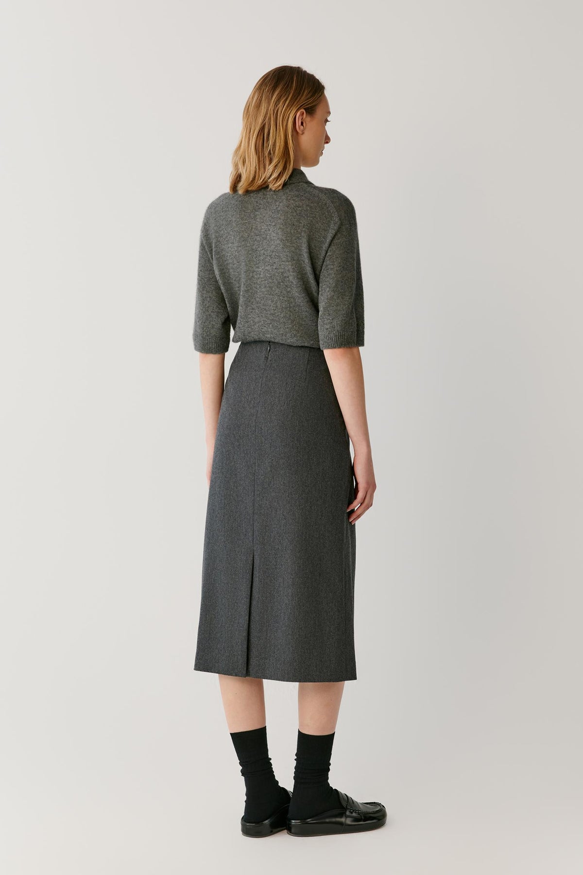 Back full-length view of a woman wearing the smoke grey cashmere and silk top, showing the straight silhouette and clean knit construction.