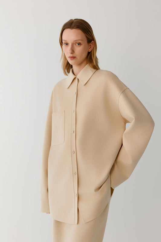 Front view of a woman wearing a beige melange double-face wool overshirt, showing the relaxed silhouette, pointed collar and concealed front fastening.
