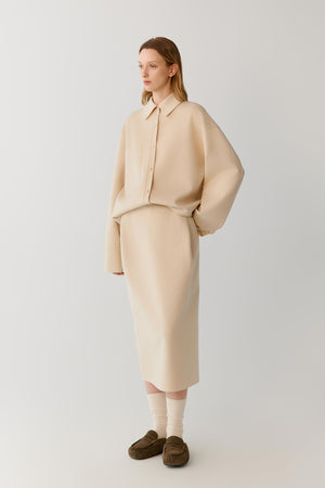 Full-length view of a woman wearing a beige melange double-face wool midi skirt, showing the straight silhouette and clean drape.