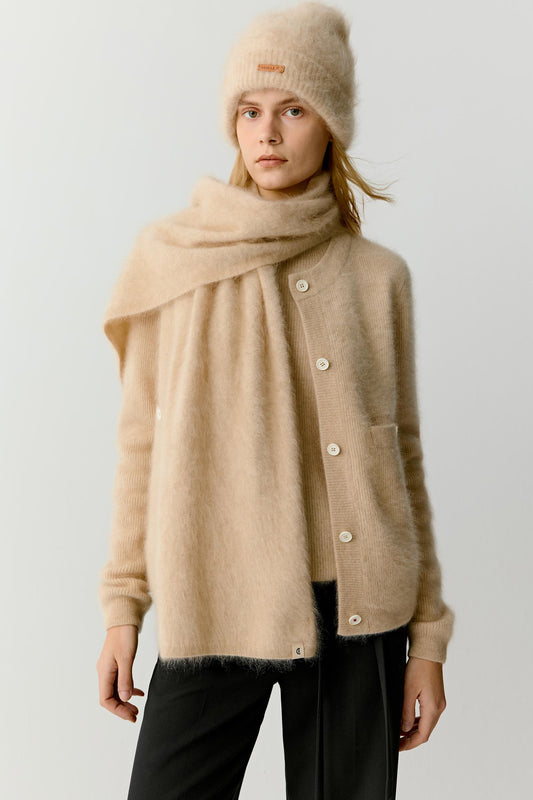 Front view of a woman wearing a beige cashmere scarf layered over a matching cardigan and dark trousers. The image highlights the plush texture, soft volume and fluid drape of the cashmere, while the generous proportions create a warm and enveloping silhouette.