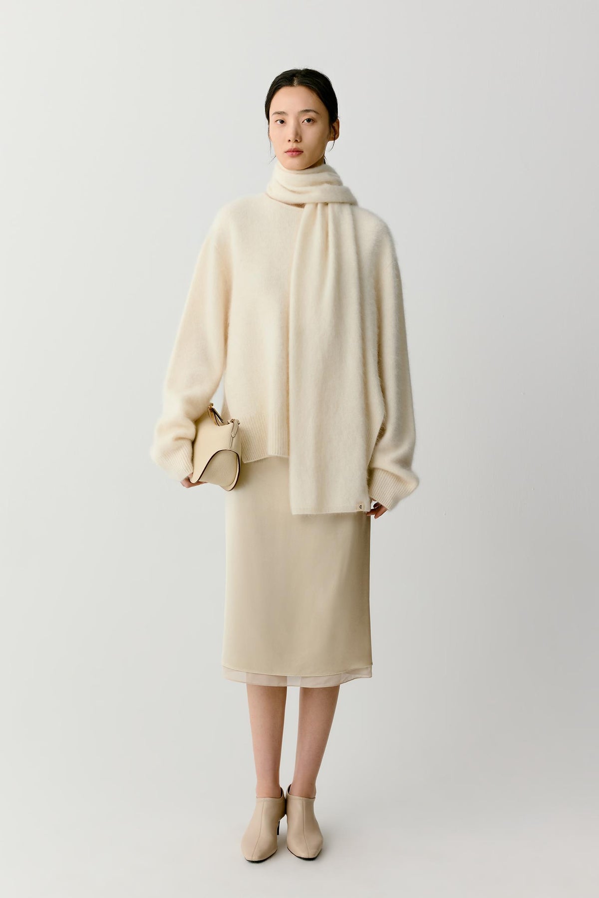 Full-length view focusing on the length and movement of the scarf. The fabric hangs with a fluid, continuous drape, revealing the soft hand and natural volume of the cashmere construction while maintaining clean, minimal lines.