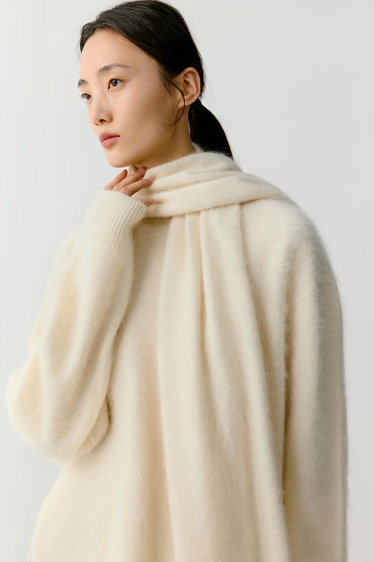 Portrait view of a woman wearing an ivory cashmere scarf draped softly around the neck and shoulders. The image highlights the plush texture, fluid drape and softly brushed surface of the cashmere, while the generous proportions create a warm and enveloping silhouette.