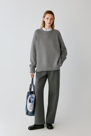Full-length view of a woman wearing grey melange wool Ponte di Roma trousers, showing the straight-leg silhouette and structured drape.