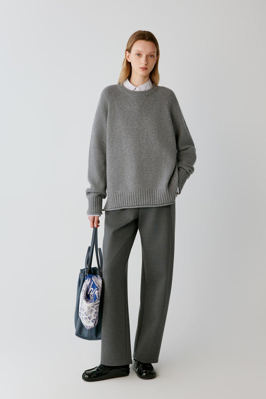 Full-length view of a woman wearing grey melange wool Ponte di Roma trousers, showing the straight-leg silhouette and structured drape.