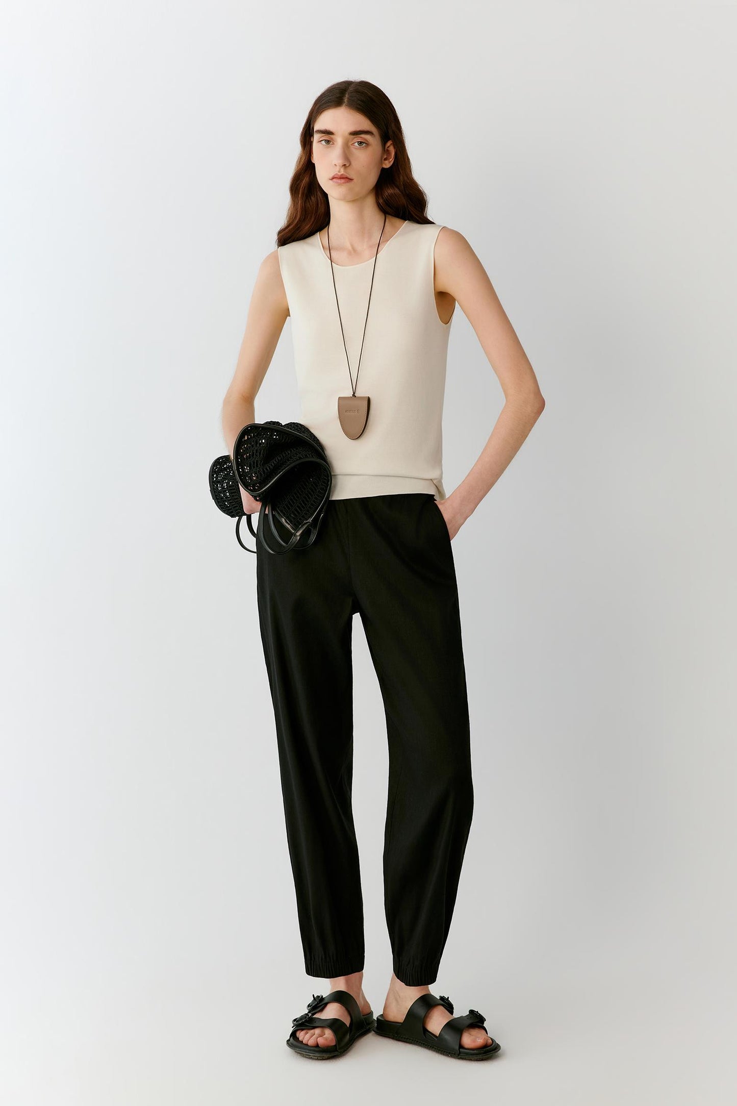 Front view of a woman wearing an ivory sleeveless top in fine-gauge silk yarn, highlighting the straight silhouette, lightweight knit construction and smooth surface. The round neckline, clean armholes and fluid drape create a refined, minimalist appearance.