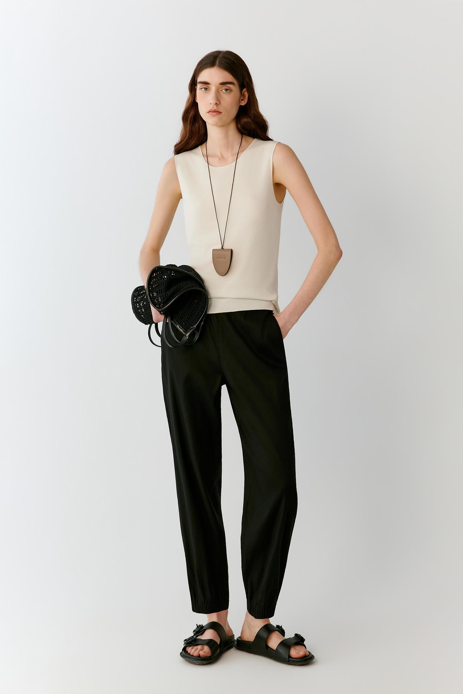 Front view of a woman wearing an ivory sleeveless top in fine-gauge silk yarn, highlighting the straight silhouette, lightweight knit construction and smooth surface. The round neckline, clean armholes and fluid drape create a refined, minimalist appearance.