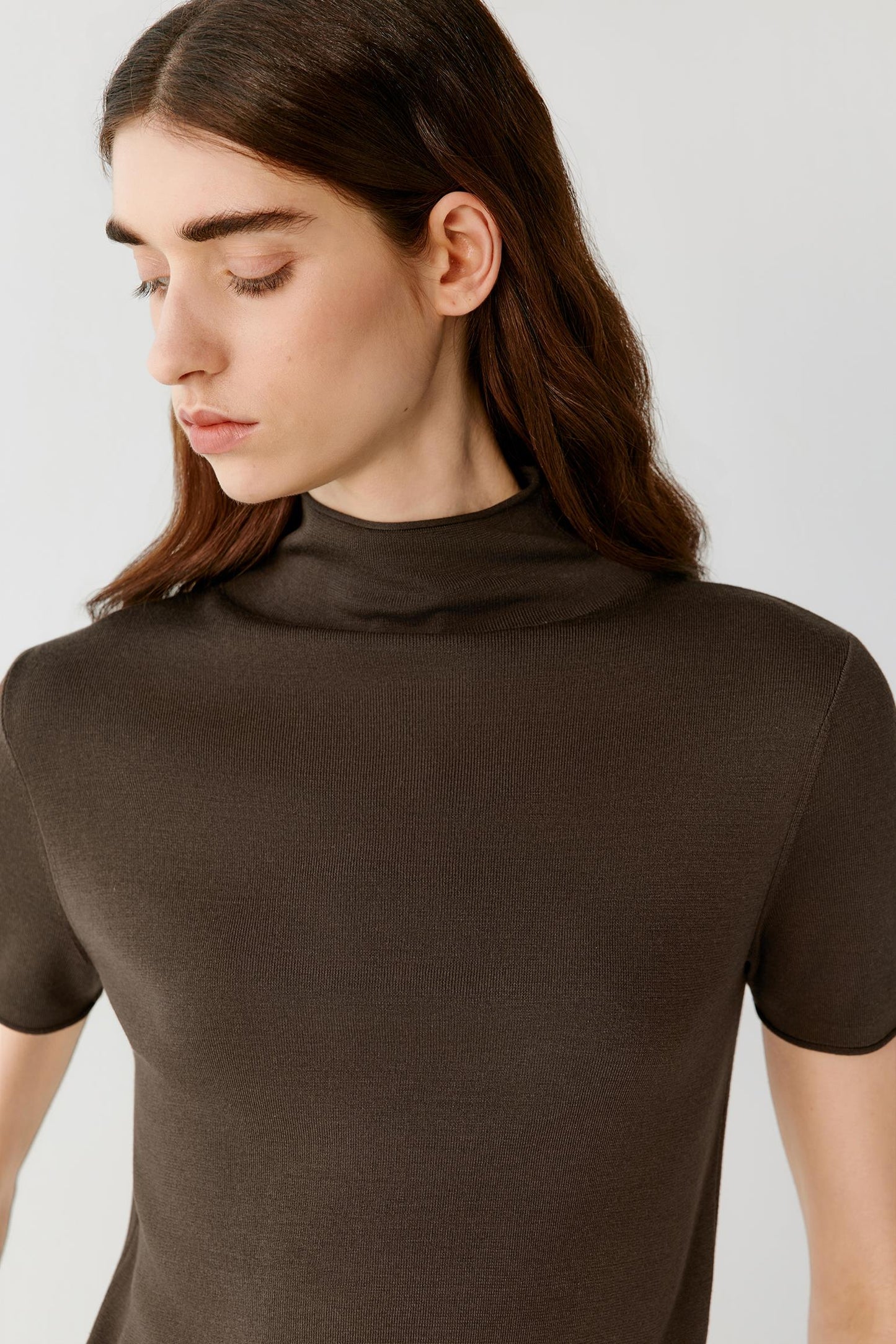 Close-up portrait focusing on the mock neckline, shoulders and upper body construction. The image reveals the smooth texture, compact knit structure and fine ribbed neckline that frame the silhouette.