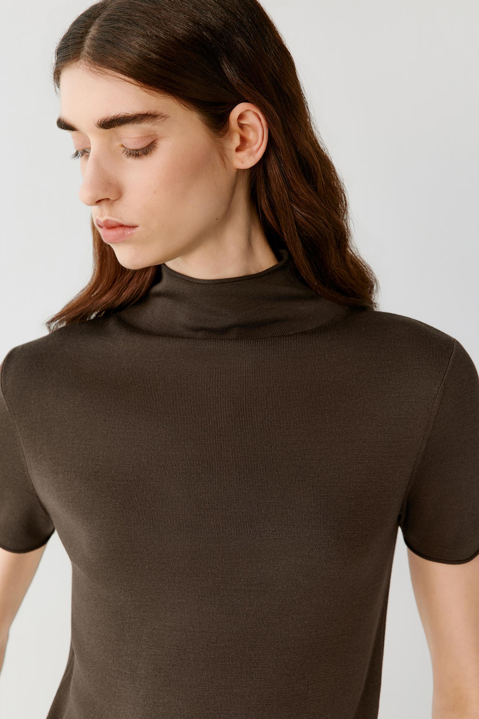 Close-up portrait focusing on the mock neckline, shoulders and upper body construction. The image reveals the smooth texture, compact knit structure and fine ribbed neckline that frame the silhouette.