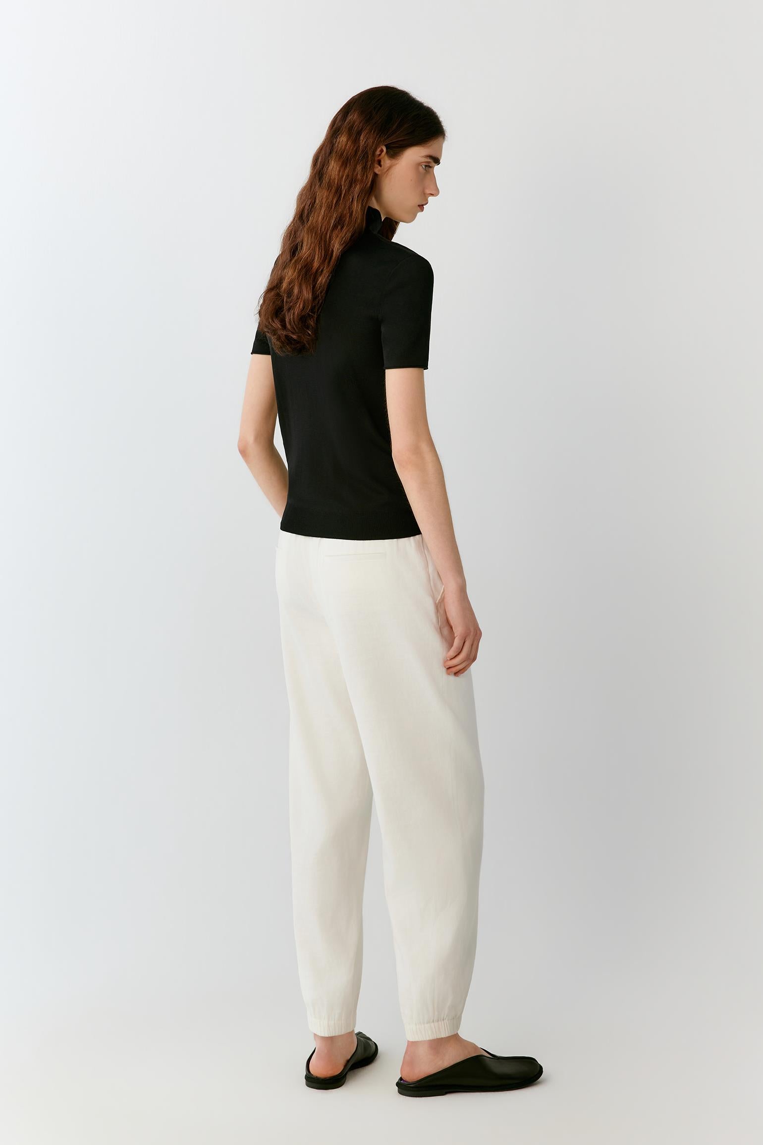 Three-quarter rear view highlighting the clean back construction, fitted silhouette and lightweight drape of the silk knit. The image emphasizes the balanced proportions and refined finishing of the garment.