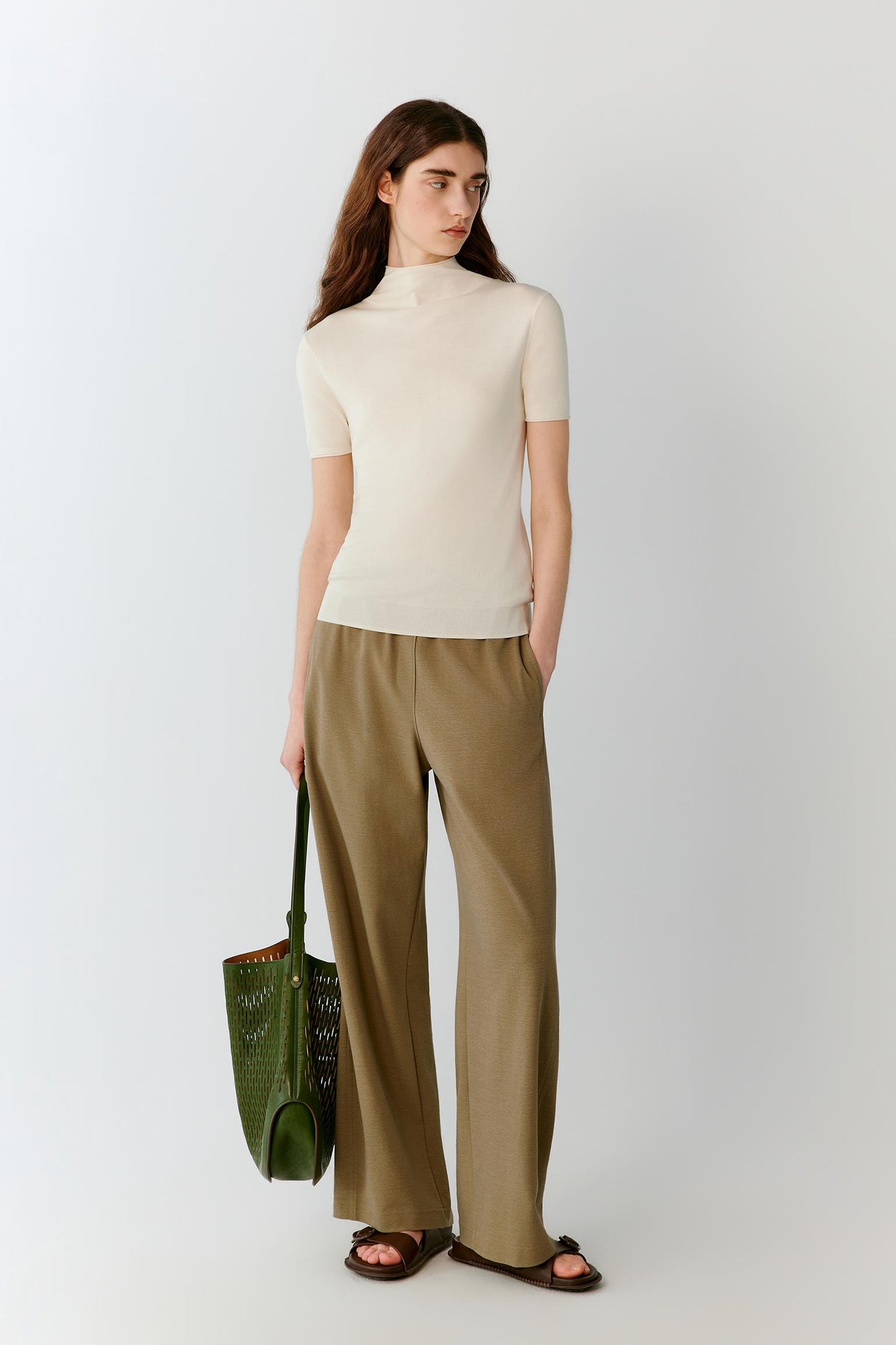 Front view of a woman wearing an ivory short-sleeved top in fine-gauge silk yarn, highlighting the fitted silhouette, lightweight knit construction and smooth, compact surface. The mock neckline, short sleeves and clean lines create a refined, minimalist appearance.