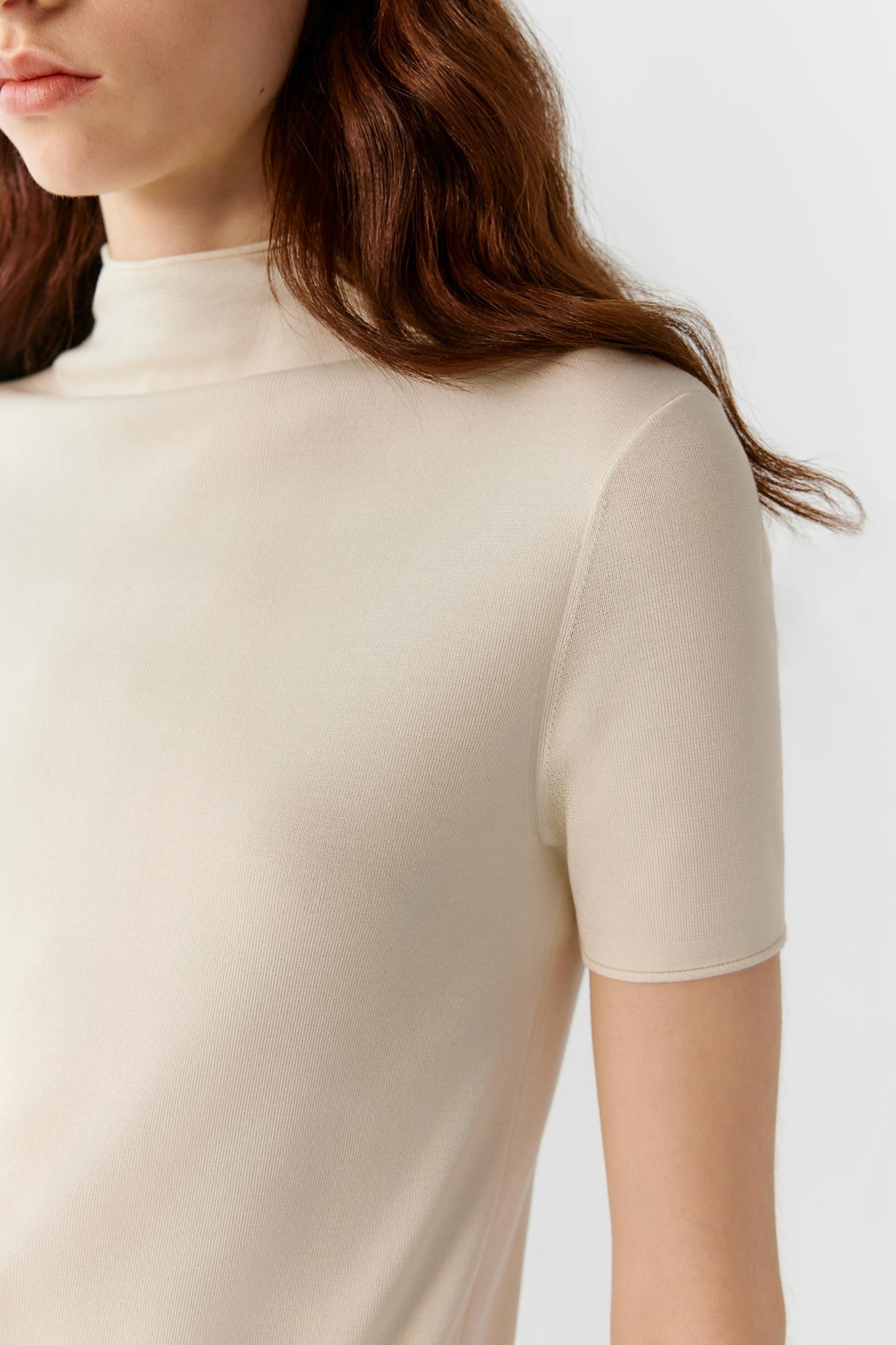 Close-up of the upper body highlighting the mock neckline, short sleeve construction and fine ribbed finishes. The image reveals the smooth, compact knit structure and the soft hand of the ivory silk yarn.