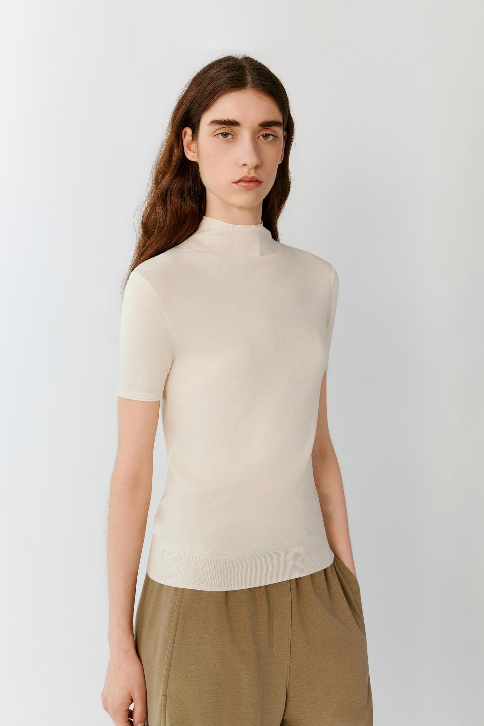 Three-quarter view showing the fitted shape and the natural drape of the fine-gauge silk knit. The image emphasizes the mock neckline, fine ribbed finishes and the clean structure of the garment.