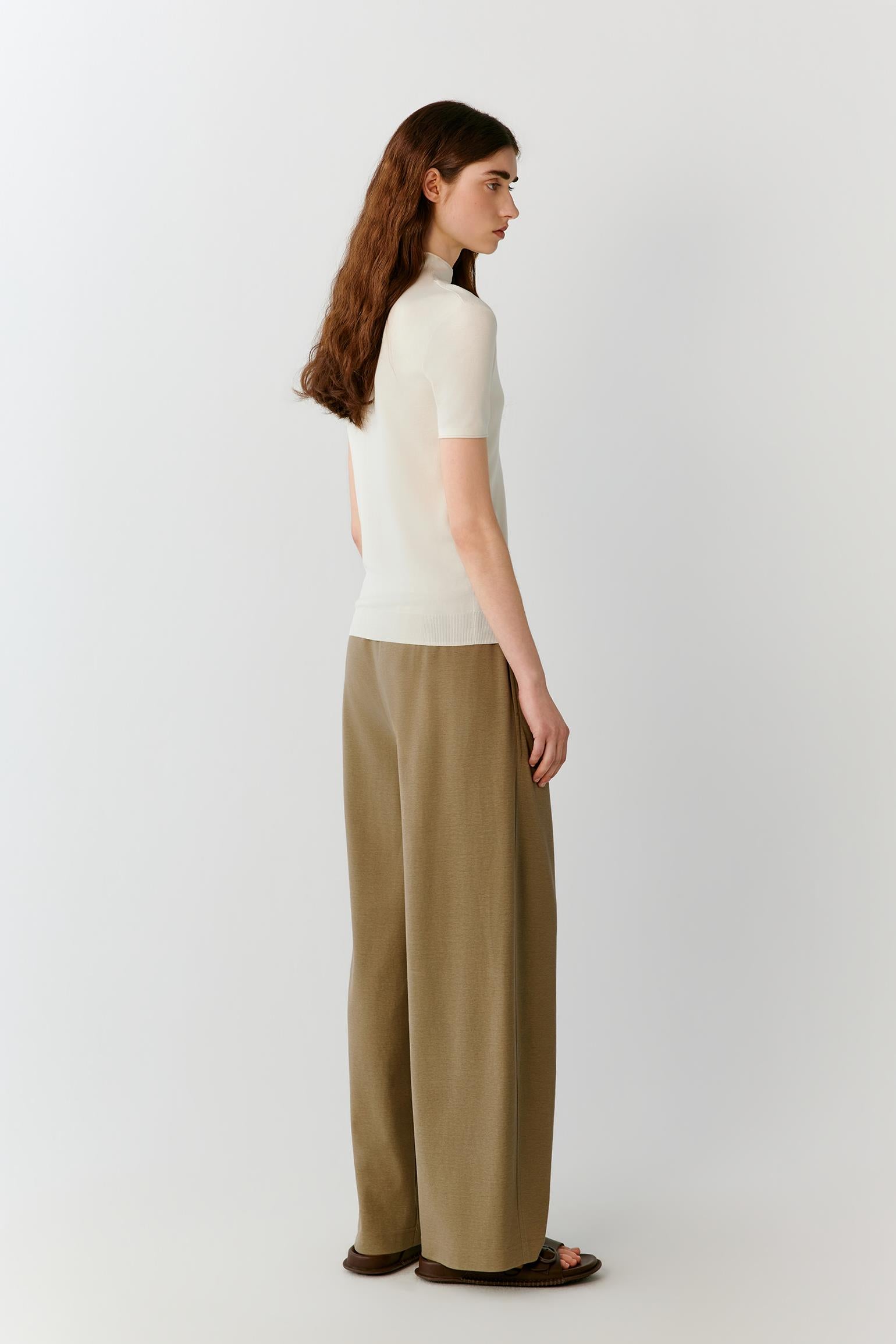 Three-quarter rear view highlighting the clean back construction, fitted silhouette and fluid drape of the fine-gauge silk knit. The image emphasizes the balanced proportions, smooth surface and understated elegance of the garment.
